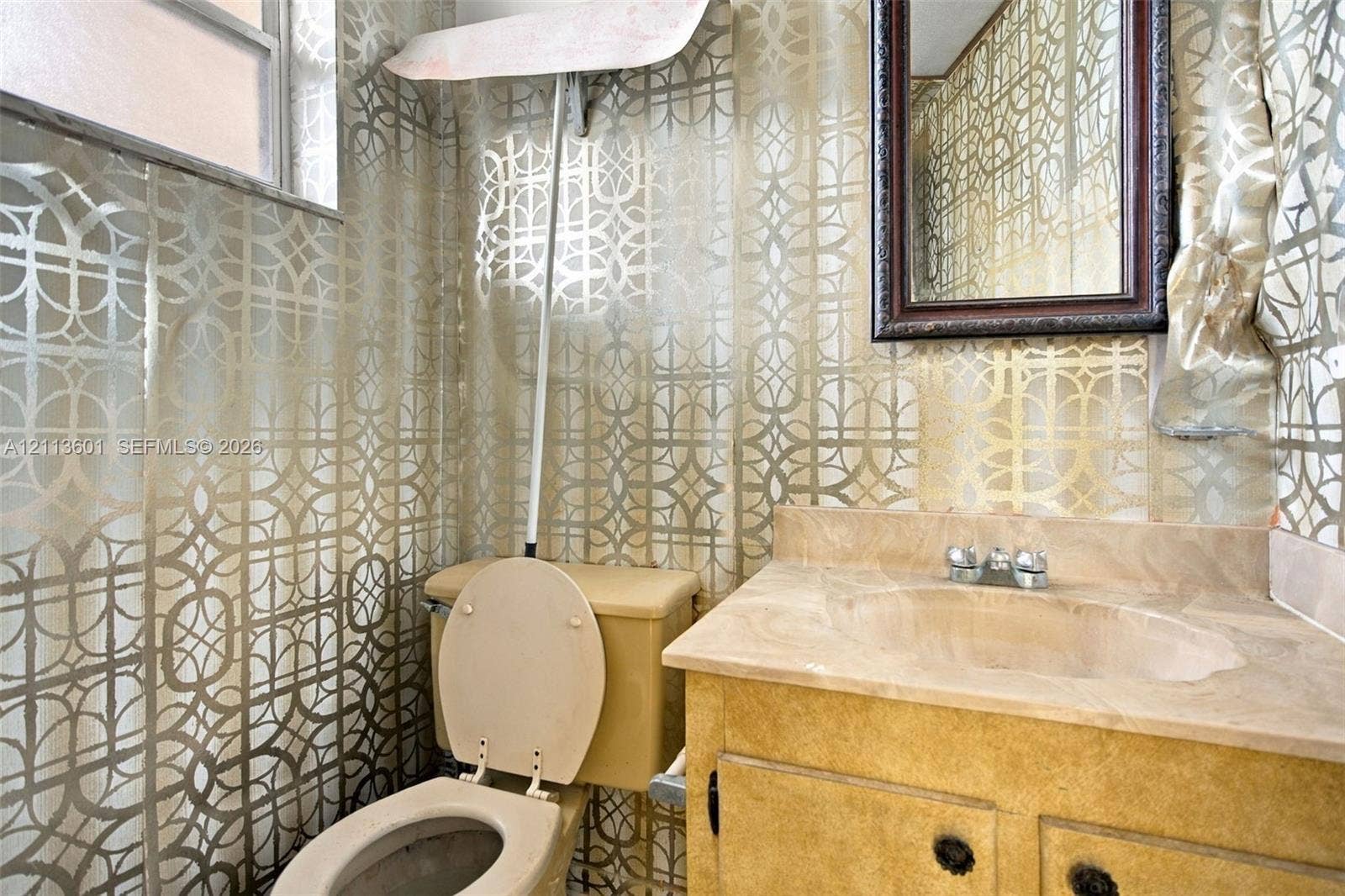 Bathroom featuring patterned metallic wallpaper, a stone-finish vanity countertop with an integrated basin, a two-handle chrome faucet, and a wall-mounted framed mirror