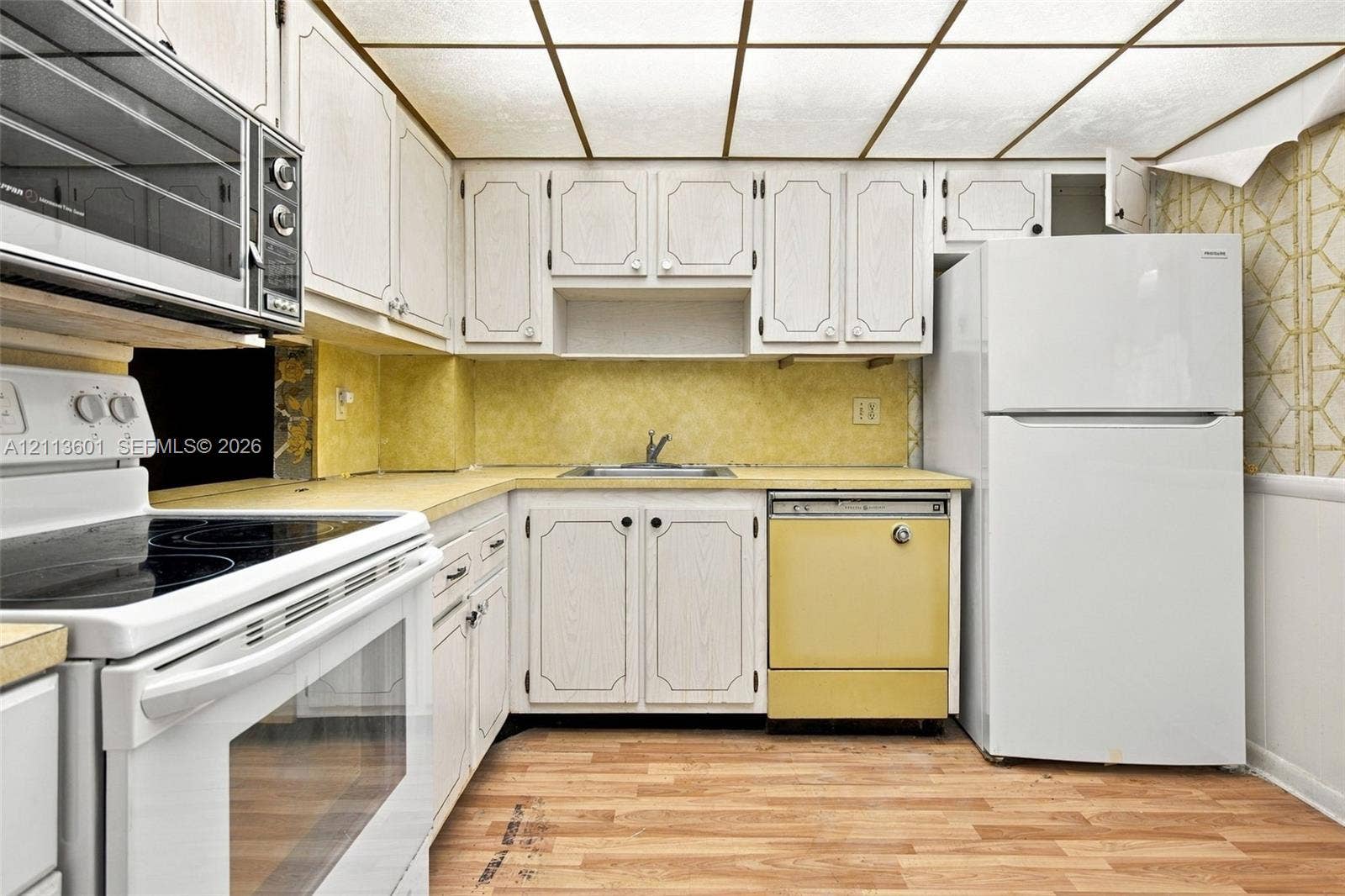 Kitchen featuring white wood-finish cabinetry, a drop-in sink, wood-finish flooring, and a grid-panel drop ceiling