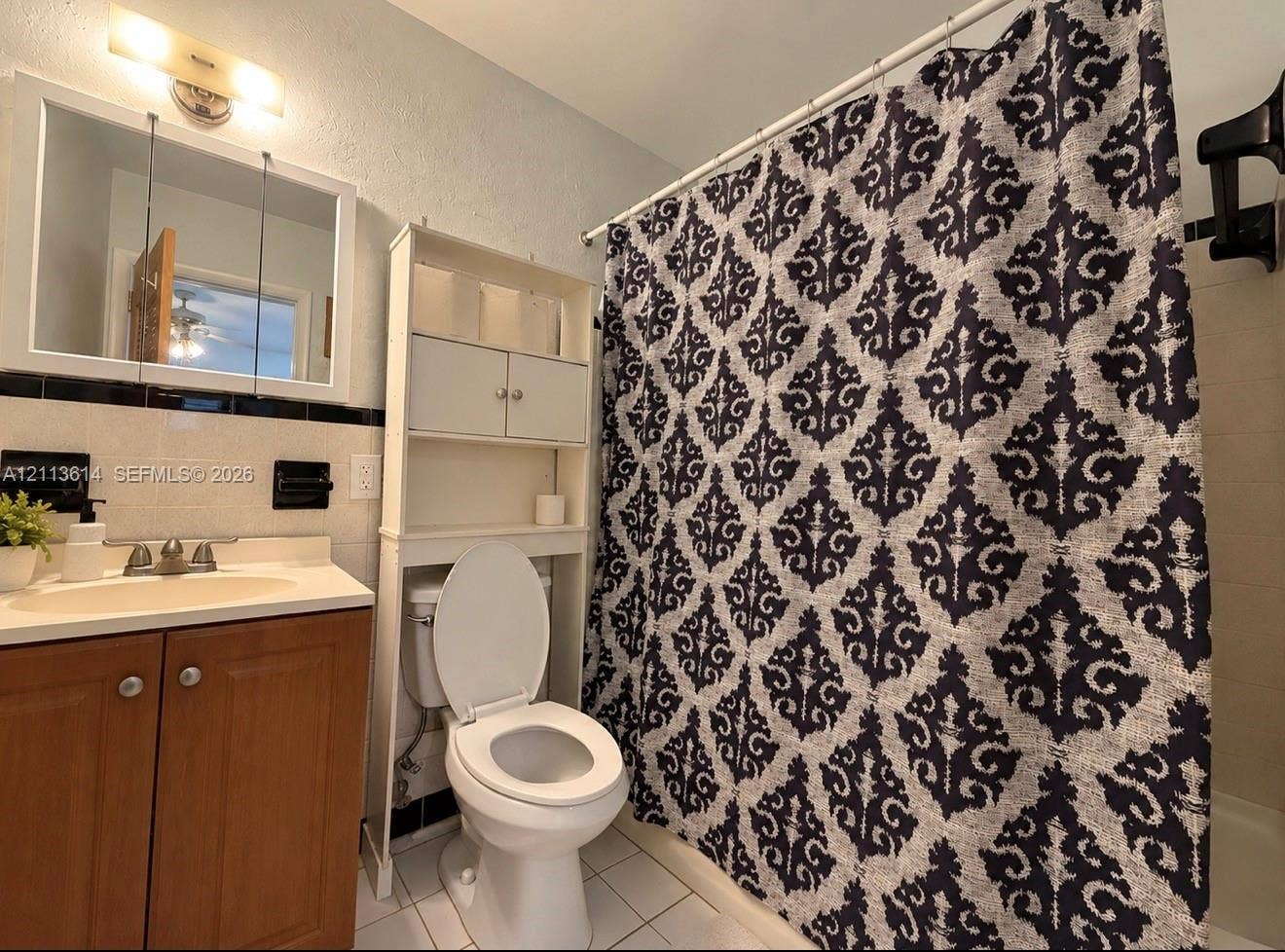 2901 Polk Street, #16, Hollywood, Hollywood, FL 33020 Bathroom featuring a wood-finish vanity, solid-surface countertop, medicine cabinet, tile wall accent with black trim, and white floor tiling