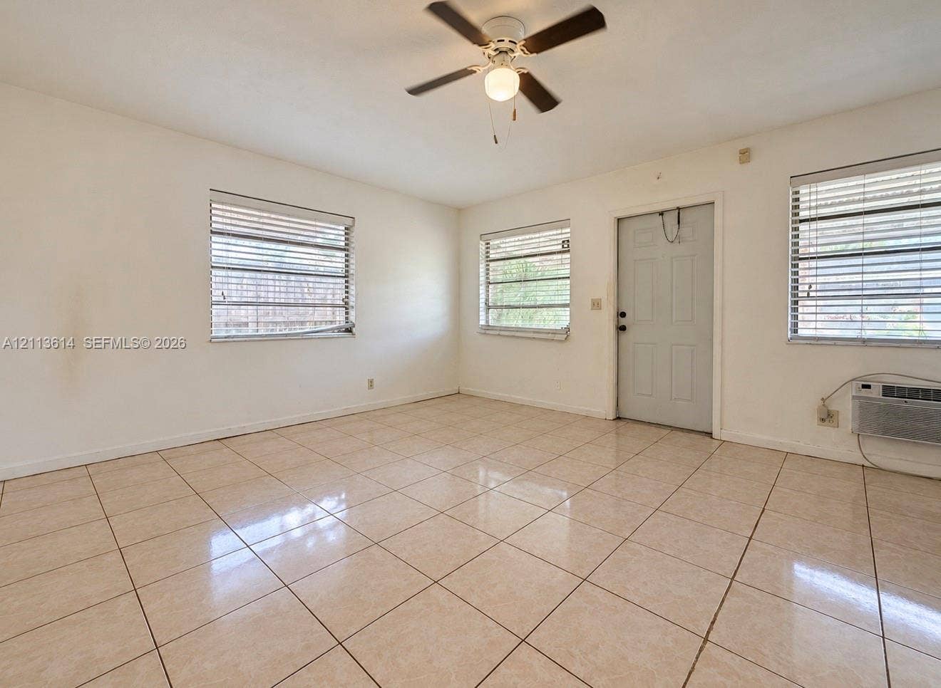 2901 Polk Street, #16, Hollywood, Hollywood, FL 33020 Neutral-toned tile flooring, three windows with horizontal blinds, a ceiling fan with integrated lighting, and a wall-mounted air conditioning unit