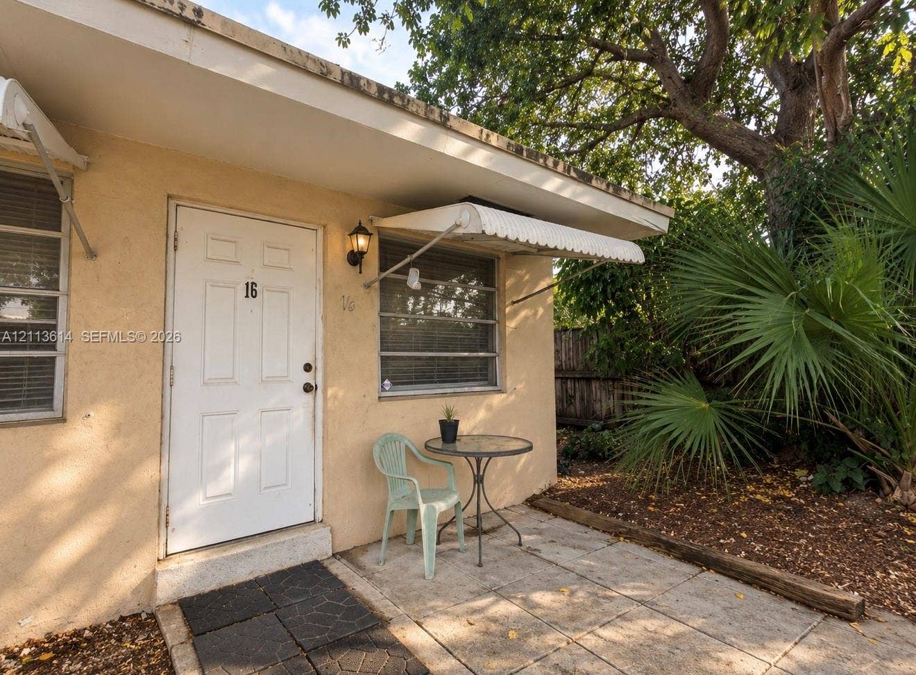 2901 Polk Street, #16, Hollywood, Hollywood, FL 33020 Stucco exterior featuring a paved stone patio, metal window awnings, wall-mounted lantern lighting, and aluminum-frame windows