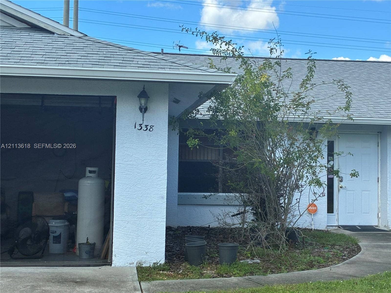 1338 Coral Reef Avenue NW, Palm Bay, FL 32907 Stucco exterior featuring a shingle roof, paved concrete walkway, wall-mounted outdoor lighting, and attached garage