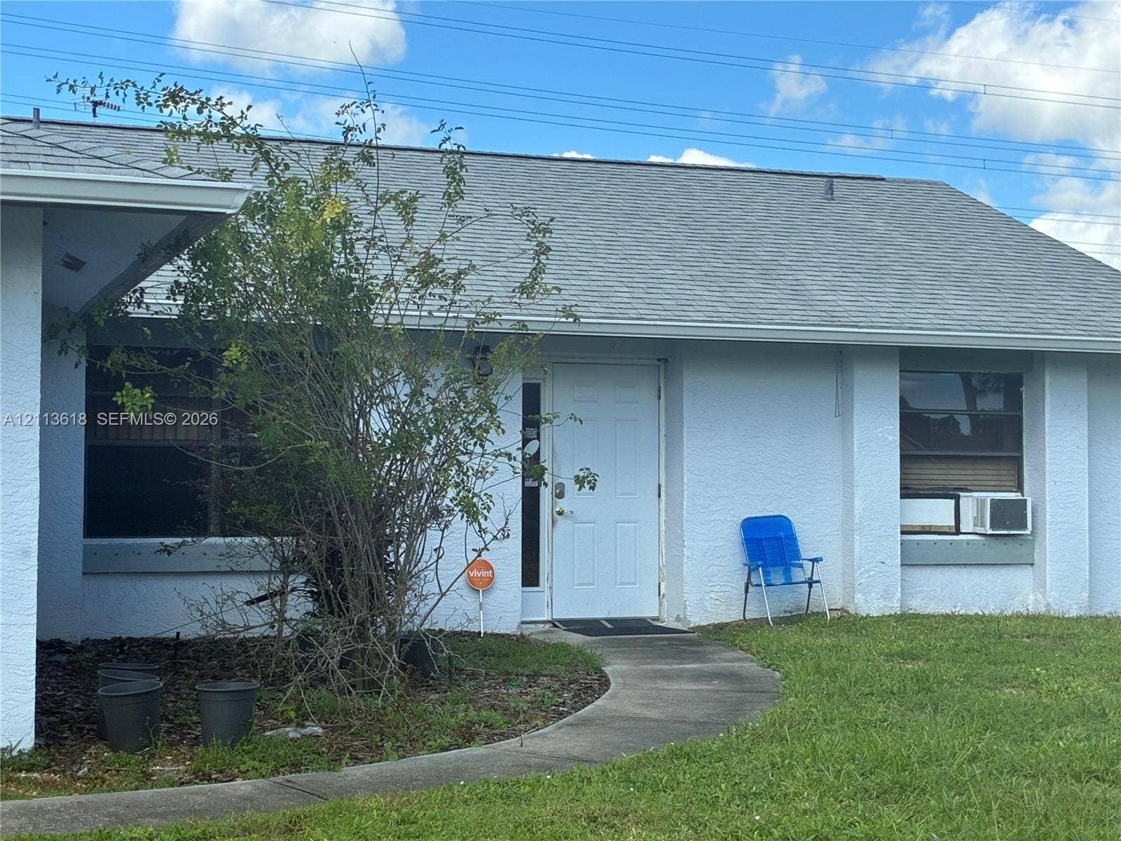 1338 Coral Reef Avenue NW, Palm Bay, FL 32907 Single-story exterior featuring light-colored textured masonry, a gabled roof with asphalt shingles, and a paved walkway