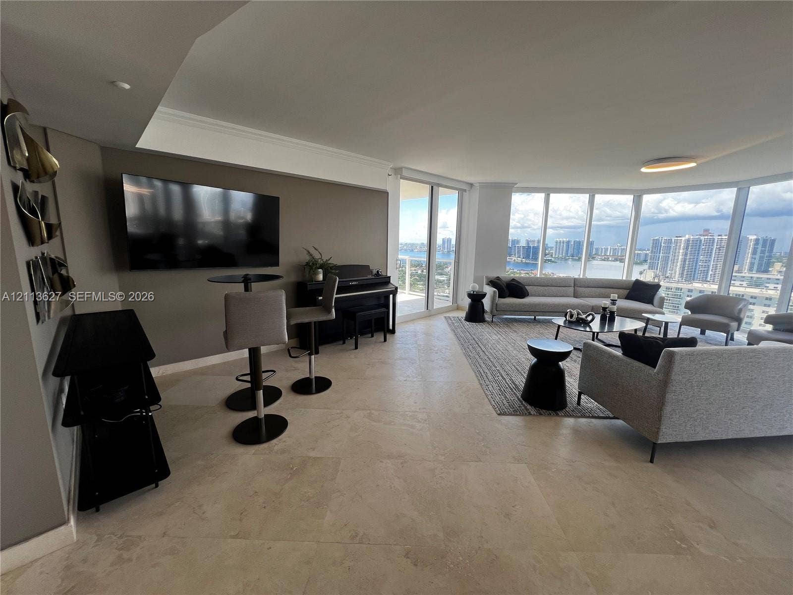 Open-concept interior featuring large-format stone tile flooring, floor-to-ceiling glass walls, and panoramic coastal and city skyline scenery