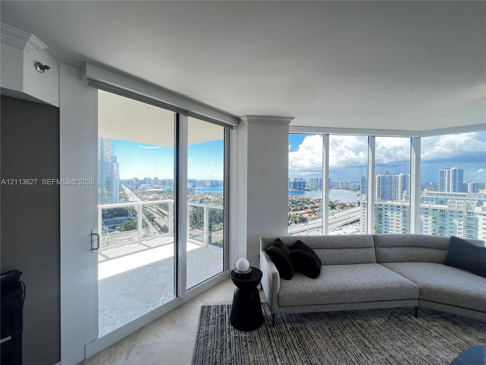 Floor-to-ceiling windows, sliding glass door, private balcony, and light-tone stone flooring
