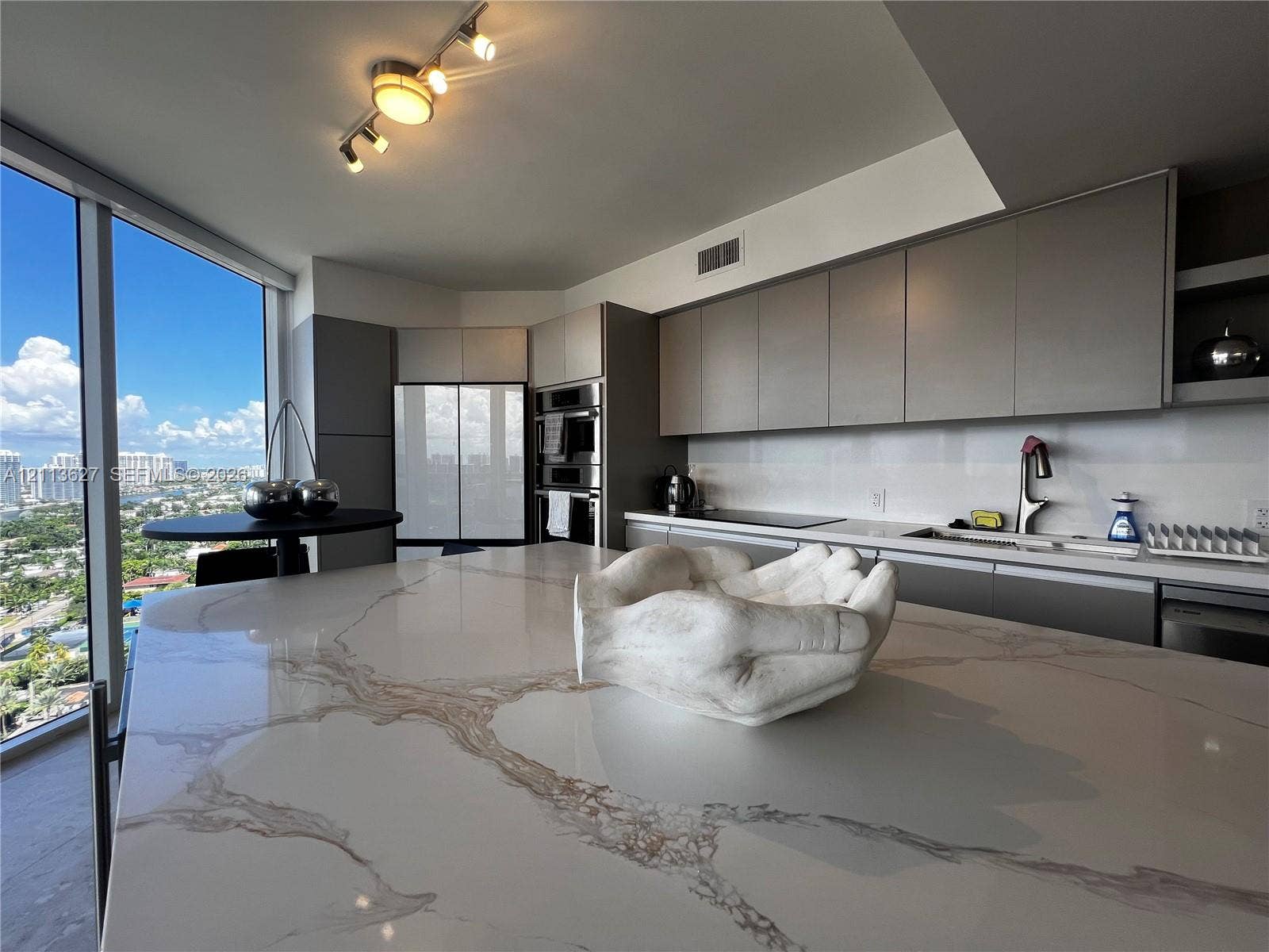 Kitchen featuring an oversized island with a stone-finish countertop, flat-panel cabinetry, integrated wall ovens, and floor-to-ceiling windows