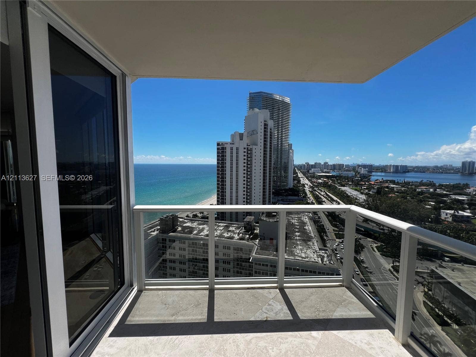 Private balcony featuring stone flooring, a white metal railing with glass panels, and sliding glass doors