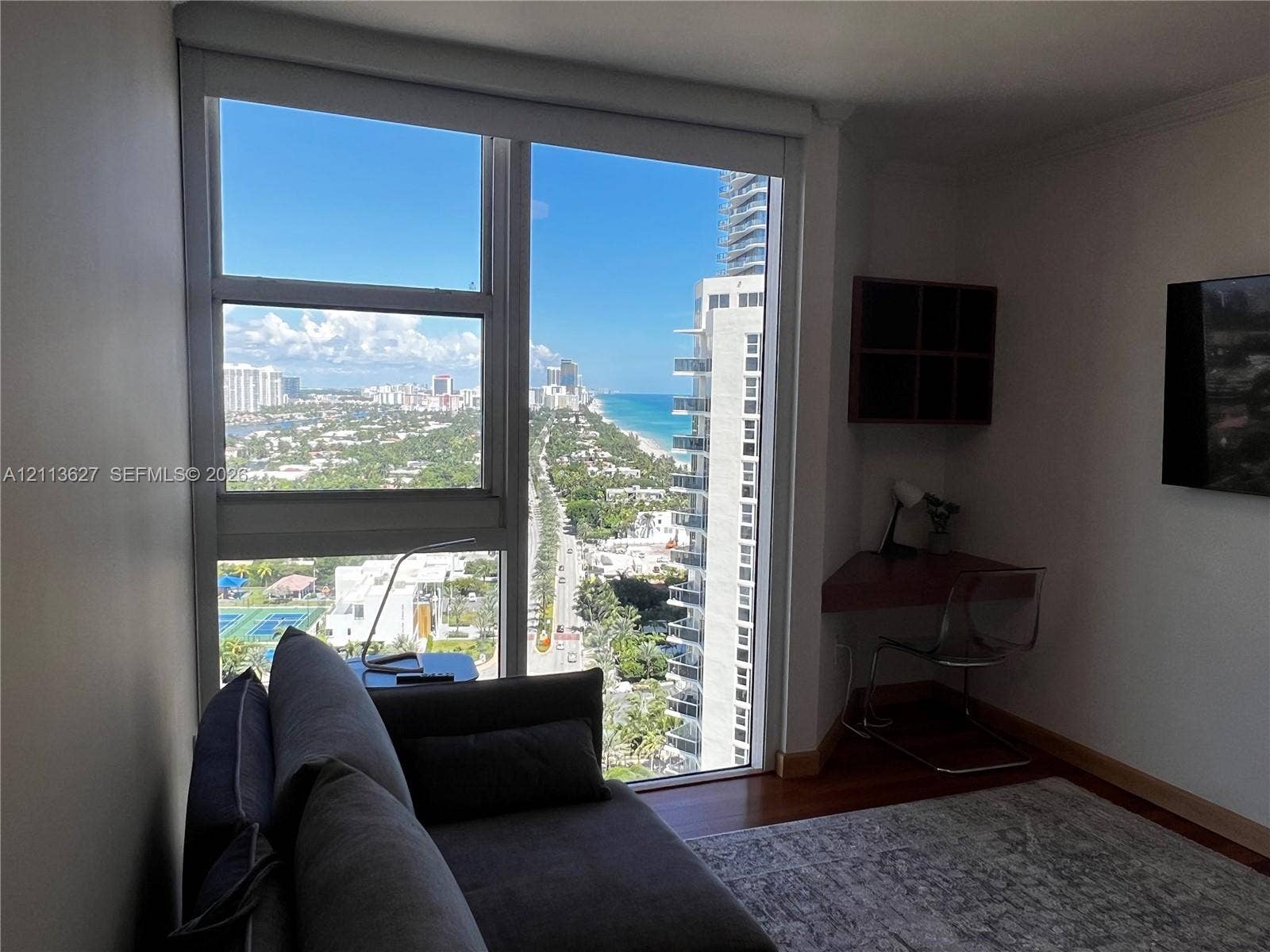 Floor-to-ceiling windows featuring coastal and urban skyline scenery, hardwood flooring, and a built-in corner desk