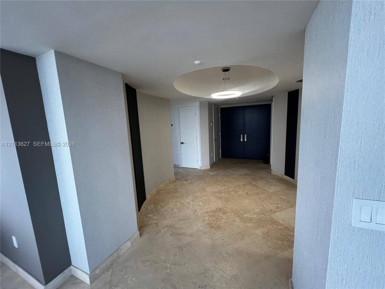 Interior space featuring large-format natural stone tile flooring, a recessed circular ceiling cove, circular LED flush-mount lighting, and solid-core double doors