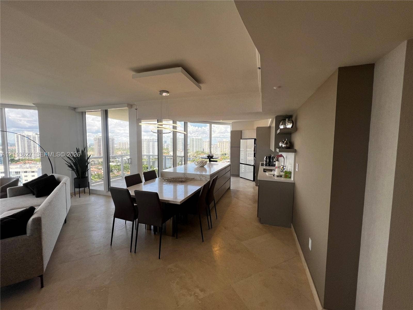 Open-concept kitchen and dining area featuring large-format stone flooring, floor-to-ceiling windows, center island with stone countertop, and built-in cabinetry