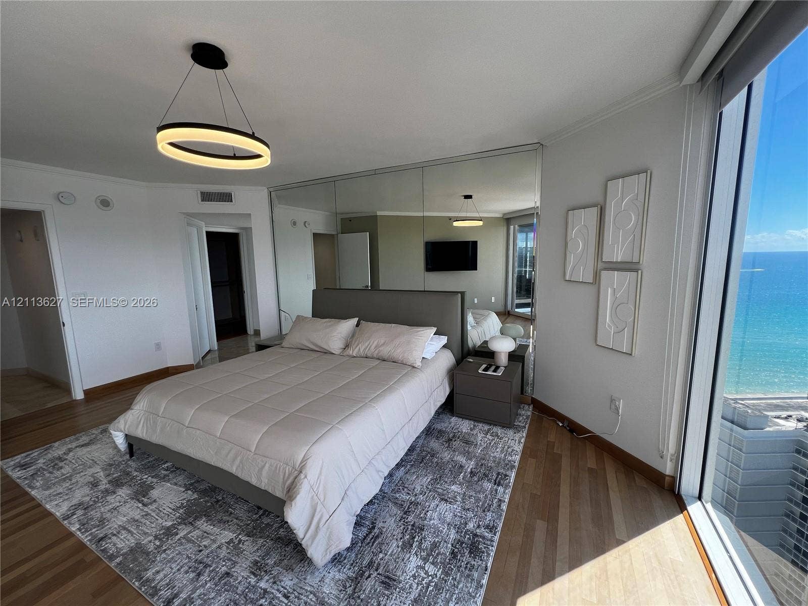 Floor-to-ceiling windows with water orientation, wood-finish flooring, full-wall mirrored accent, and contemporary circular pendant lighting