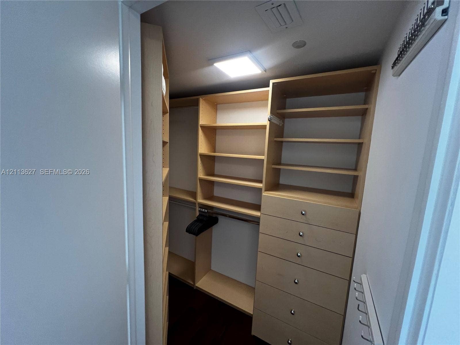 Custom walk-in closet featuring light-toned wooden shelving, integrated drawer stack with metal hardware, and recessed lighting