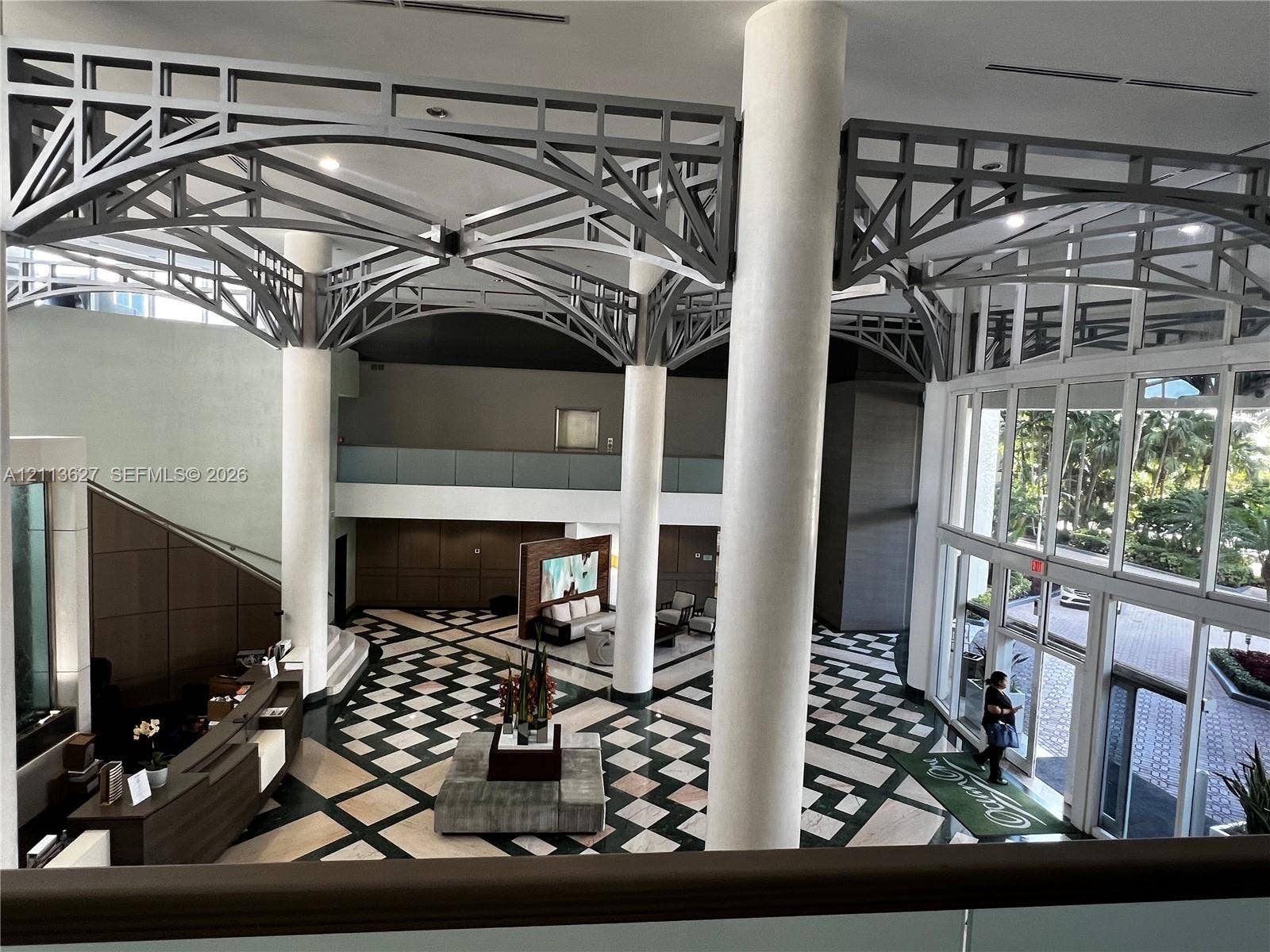 Grand foyer featuring vaulted structural steel ceiling trusses, floor-to-ceiling windows, polished stone flooring in a geometric pattern, and prominent cylindrical columns