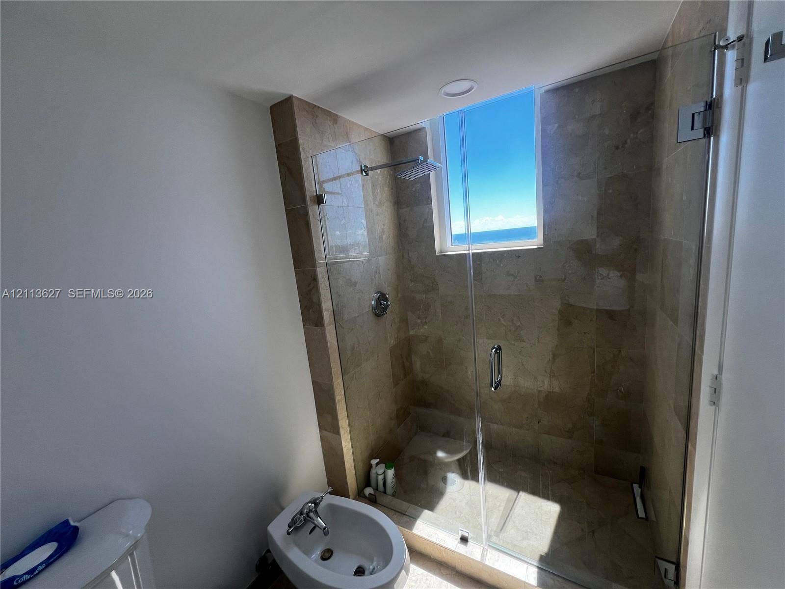Walk-in shower featuring tile surround, glass enclosure, and built-in bench, complemented by a bidet and natural light from an integrated window