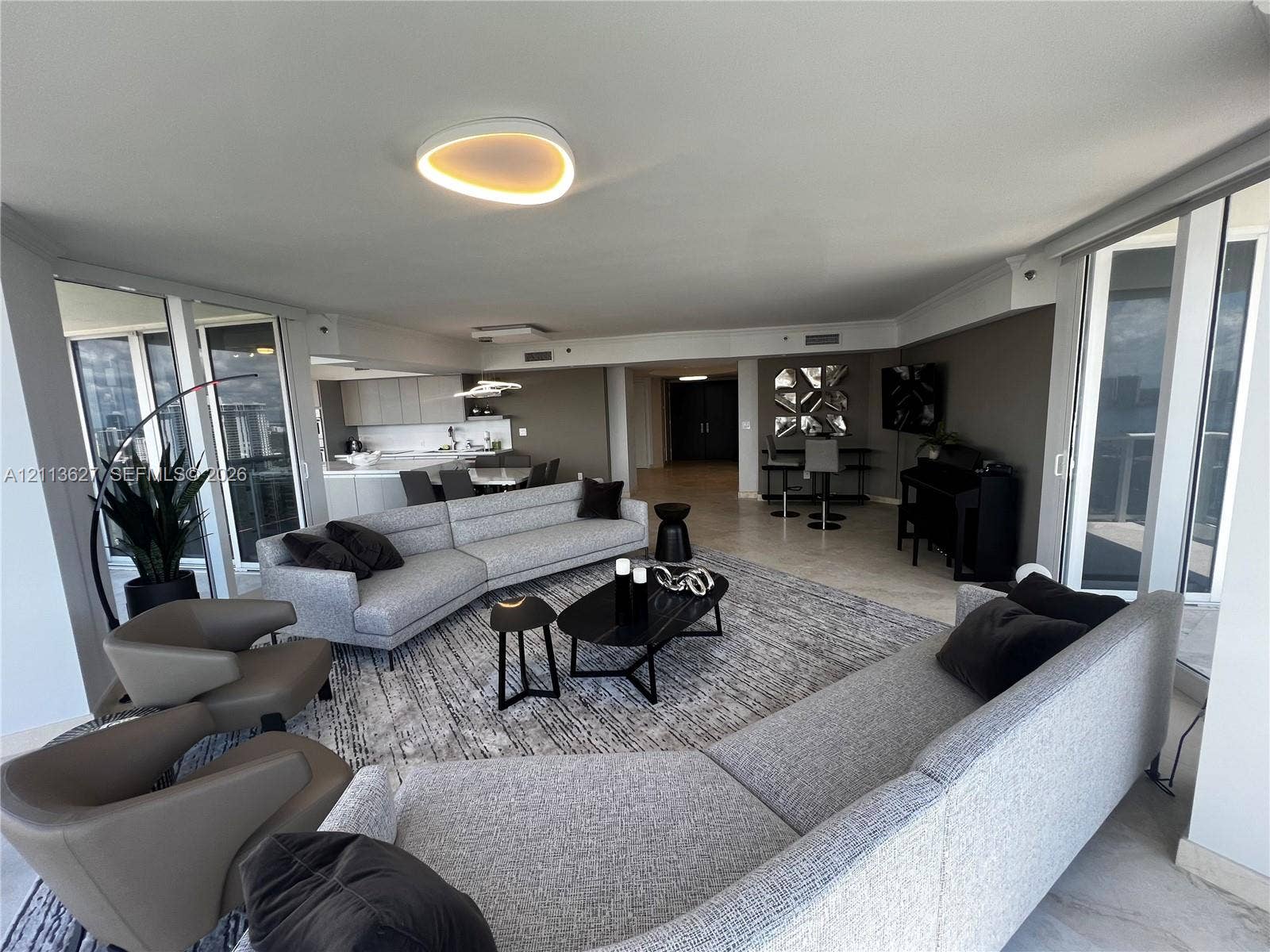 Open-concept living area featuring stone-finish flooring, floor-to-ceiling glass panel doors, custom recessed ceiling lighting, and minimalist built-in cabinetry
