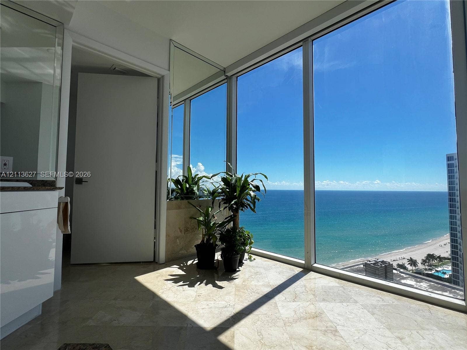 Floor-to-ceiling windows featuring ocean and coastline scenery, stone tile flooring, and a mirrored wall accent