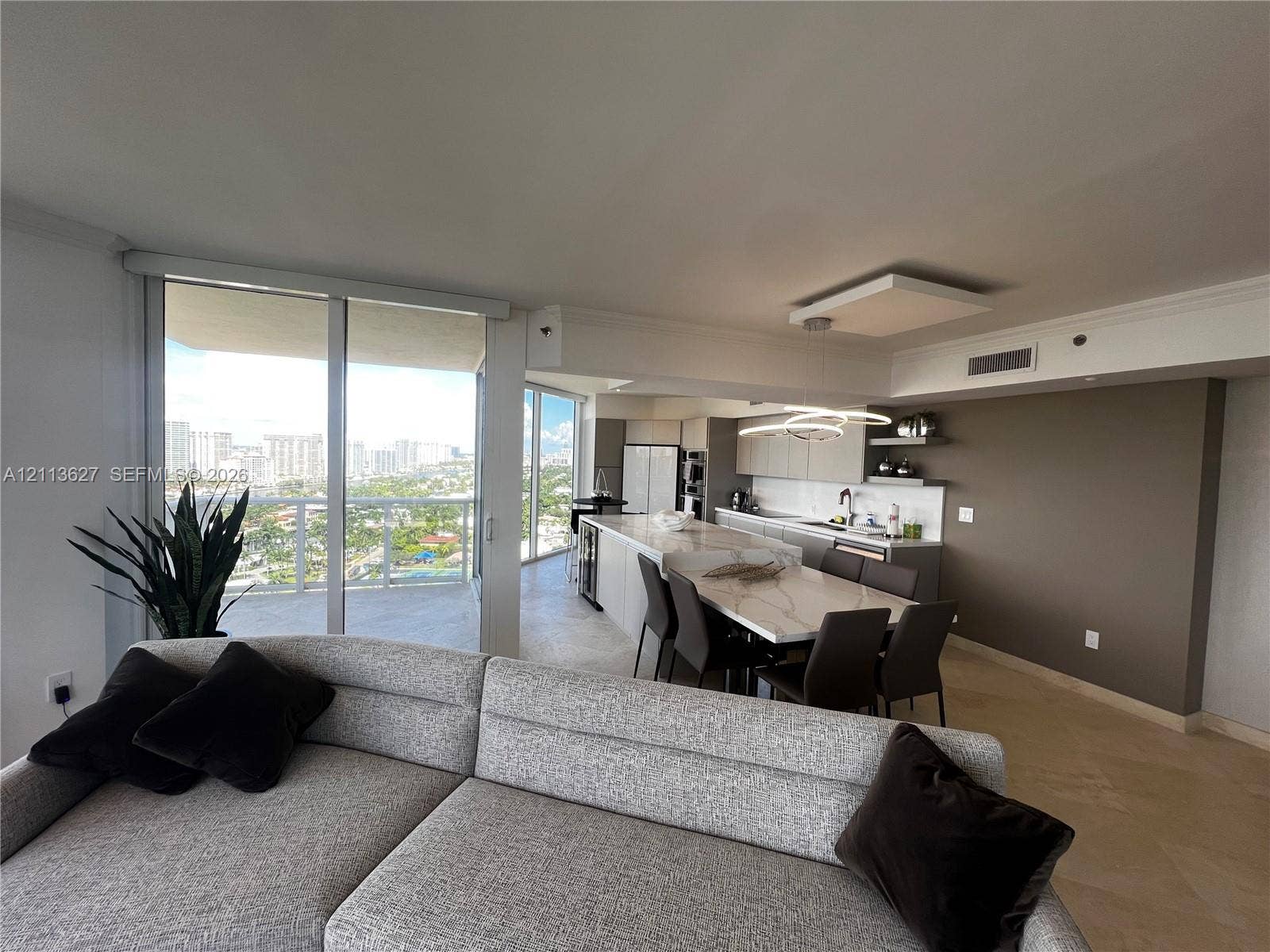 Open-concept kitchen featuring an oversized island with stone-finish countertops, flat-panel cabinetry, built-in stainless steel appliances, and floor-to-ceiling glass sliding doors