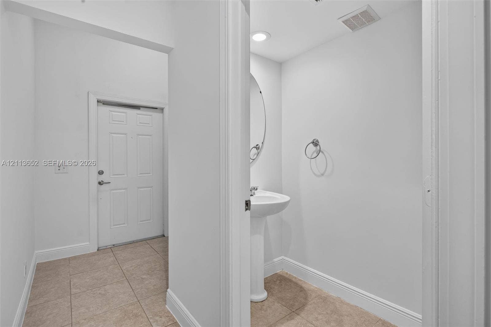 618 SW 1st Lane, Pompano Beach, FL 33060 Neutral-toned ceramic tile flooring, pedestal sink with chrome faucet, circular wall-mounted mirror, and six-panel interior door