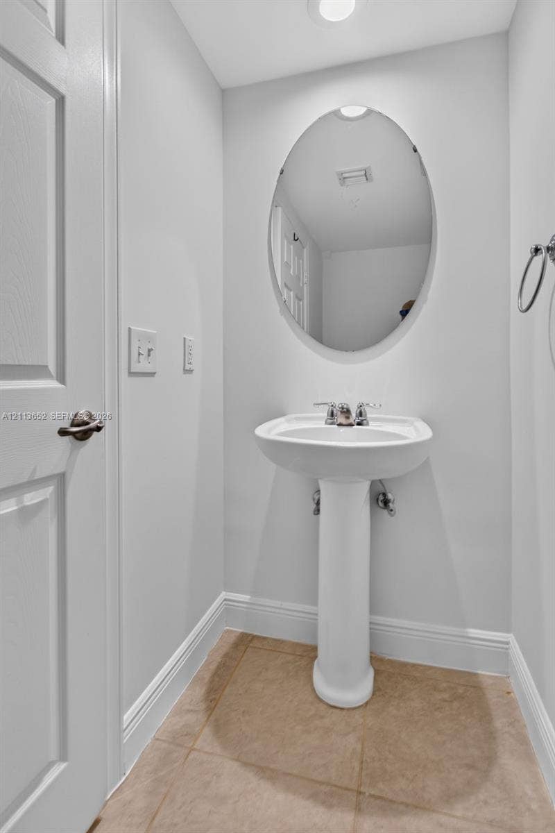 618 SW 1st Lane, Pompano Beach, FL 33060 White pedestal sink featuring a chrome dual-handle faucet, oval wall-mounted mirror, and tile flooring