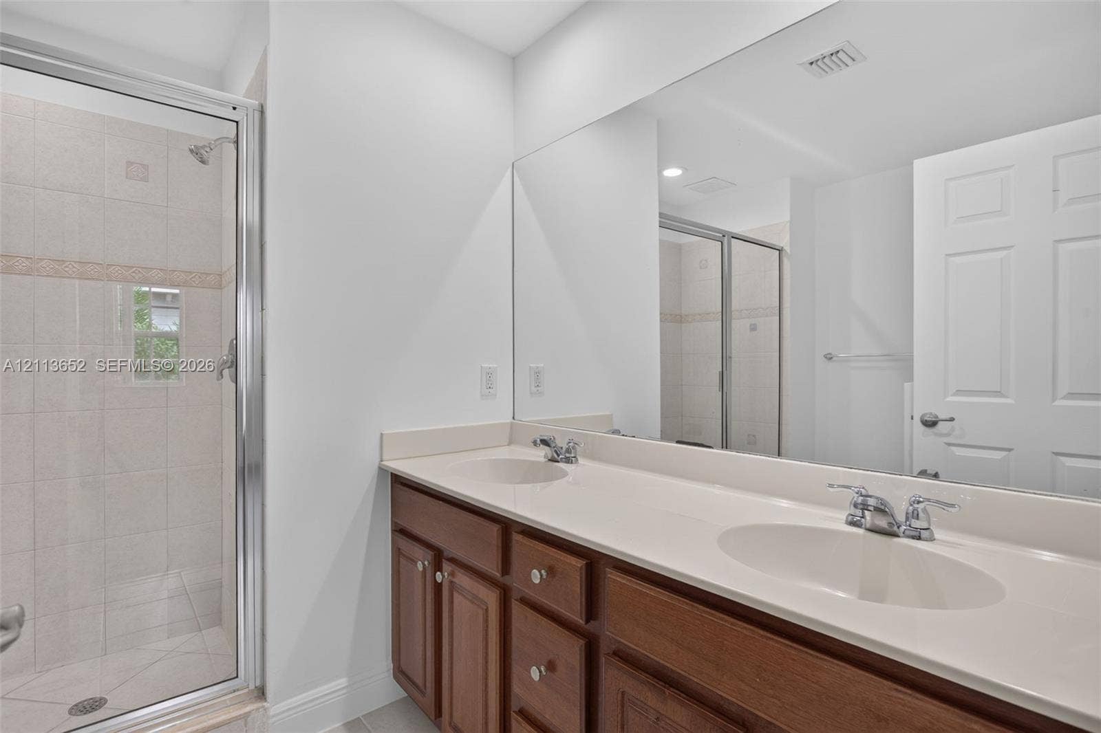 618 SW 1st Lane, Pompano Beach, FL 33060 Double vanity with integrated sinks, neutral countertop, wood cabinetry, and a full-width wall mirror, alongside a walk-in shower with tiled surround and glass enclosure