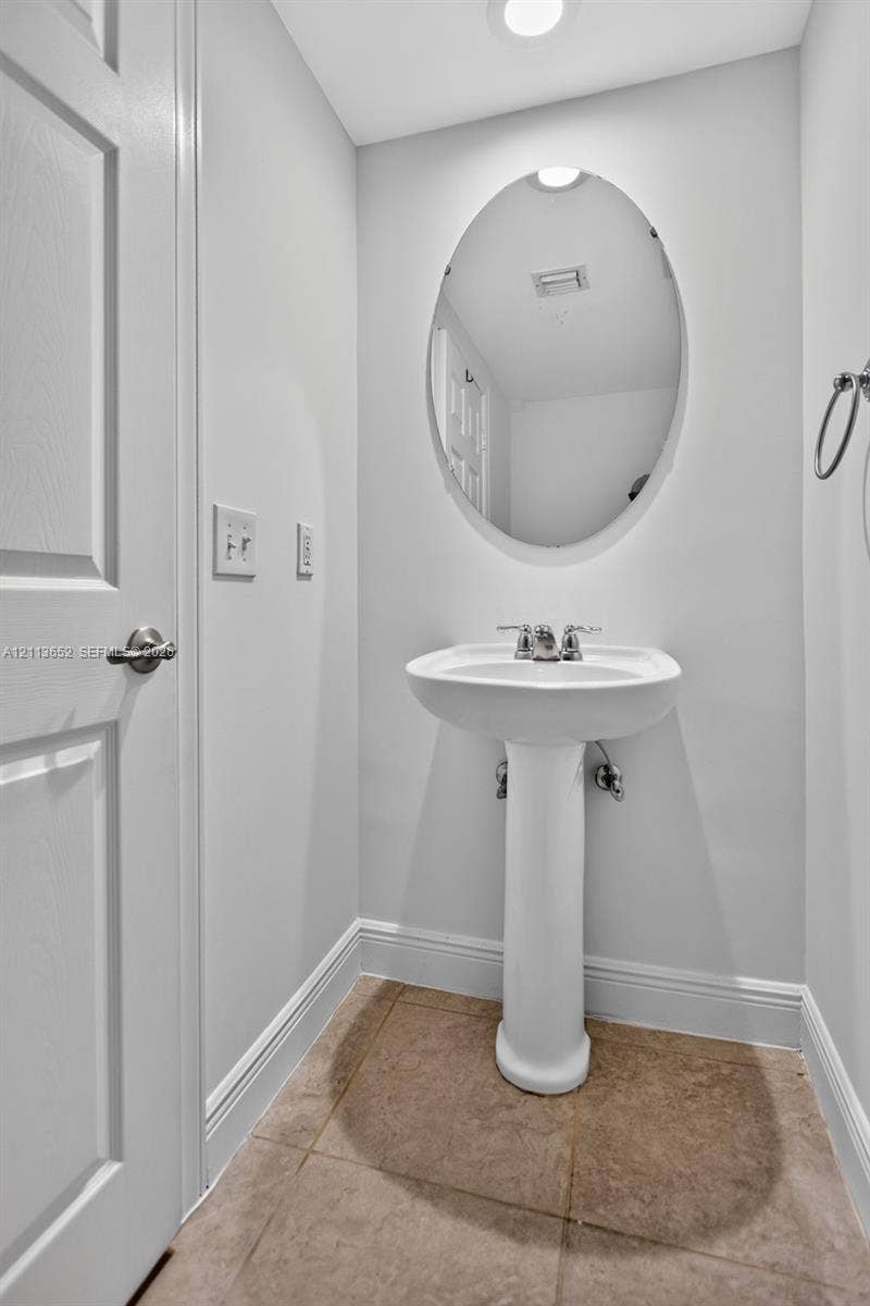 618 SW 1st Lane, Pompano Beach, FL 33060 White porcelain pedestal sink, oval wall-mounted mirror, metal faucet hardware, and neutral tile flooring