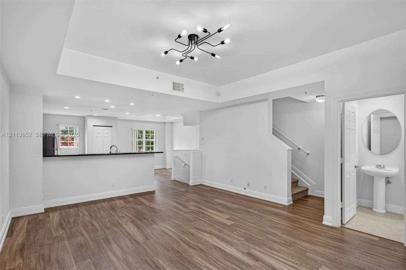618 SW 1st Lane, Pompano Beach, FL 33060 Open-concept interior featuring wood-finish flooring, a multi-arm modern chandelier, tray ceilings, and a powder room with a pedestal sink and circular mirror