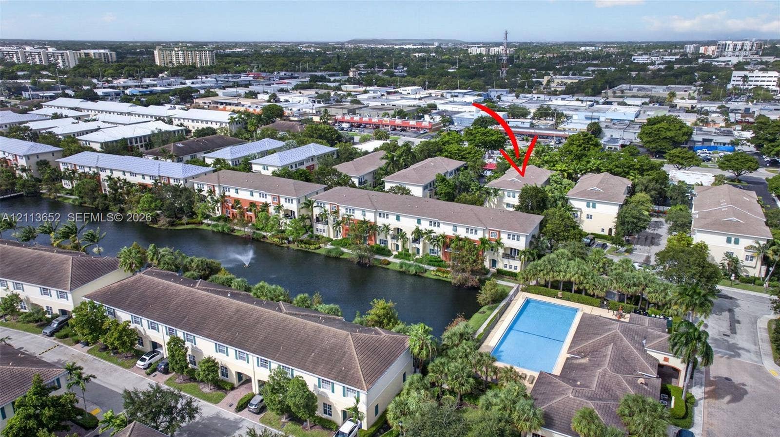 618 SW 1st Lane, Pompano Beach, FL 33060 Aerial perspective featuring a multi-story residential building with a tile roof, situated along a water feature with a fountain, including a communal swimming pool and landscaped grounds