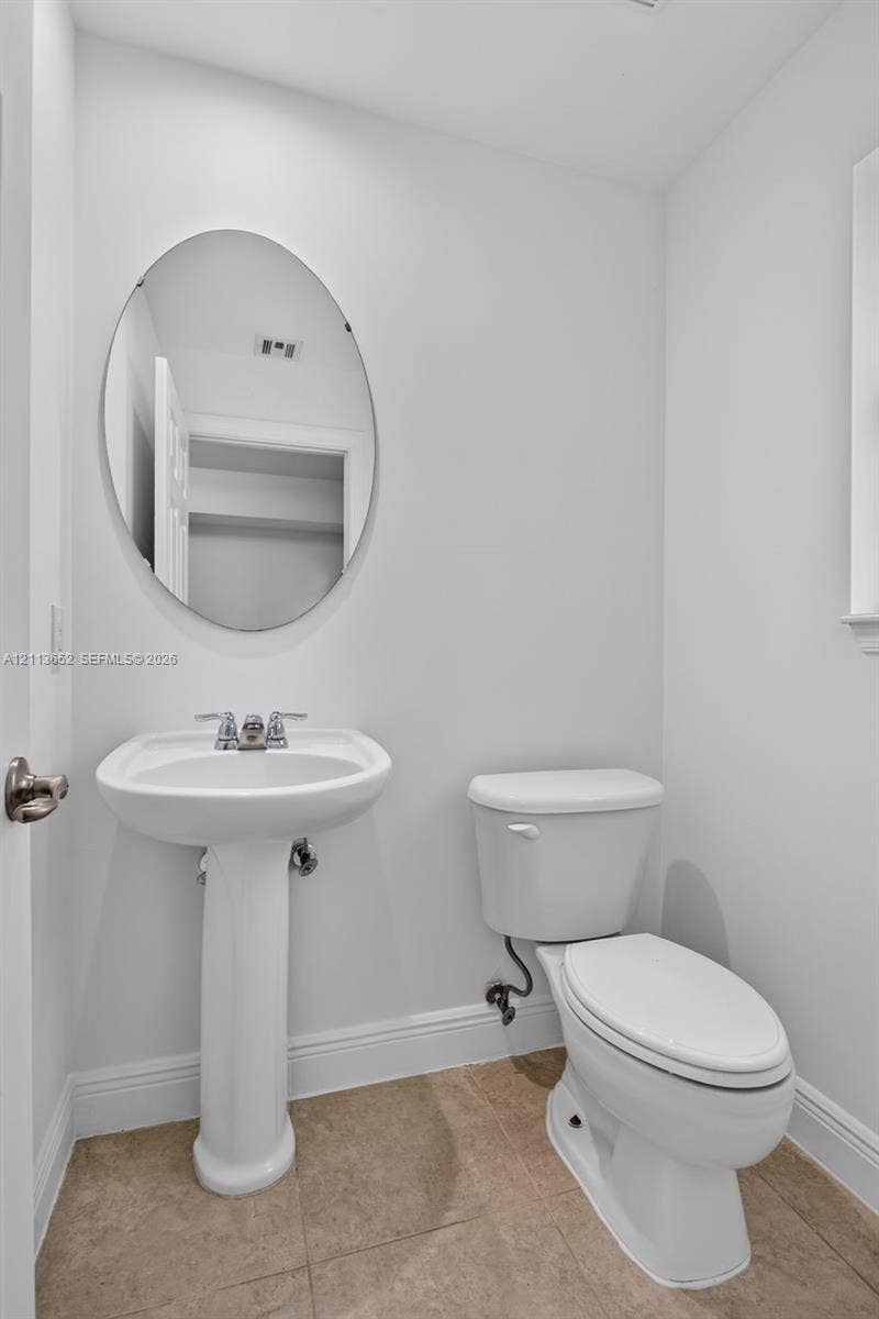 618 SW 1st Lane, Pompano Beach, FL 33060 Ceramic tile flooring, white pedestal sink with chrome faucet, oval wall-mounted mirror, and standard porcelain toilet