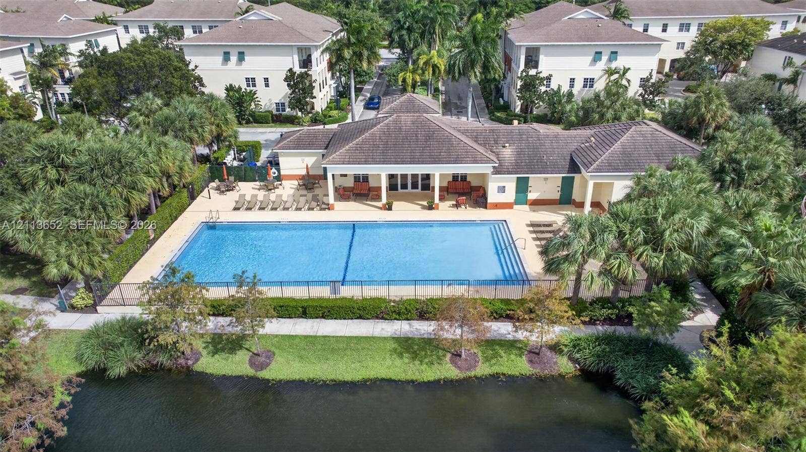 618 SW 1st Lane, Pompano Beach, FL 33060 Community swimming pool featuring a concrete deck and perimeter fencing, situated near a pond with mature landscaping