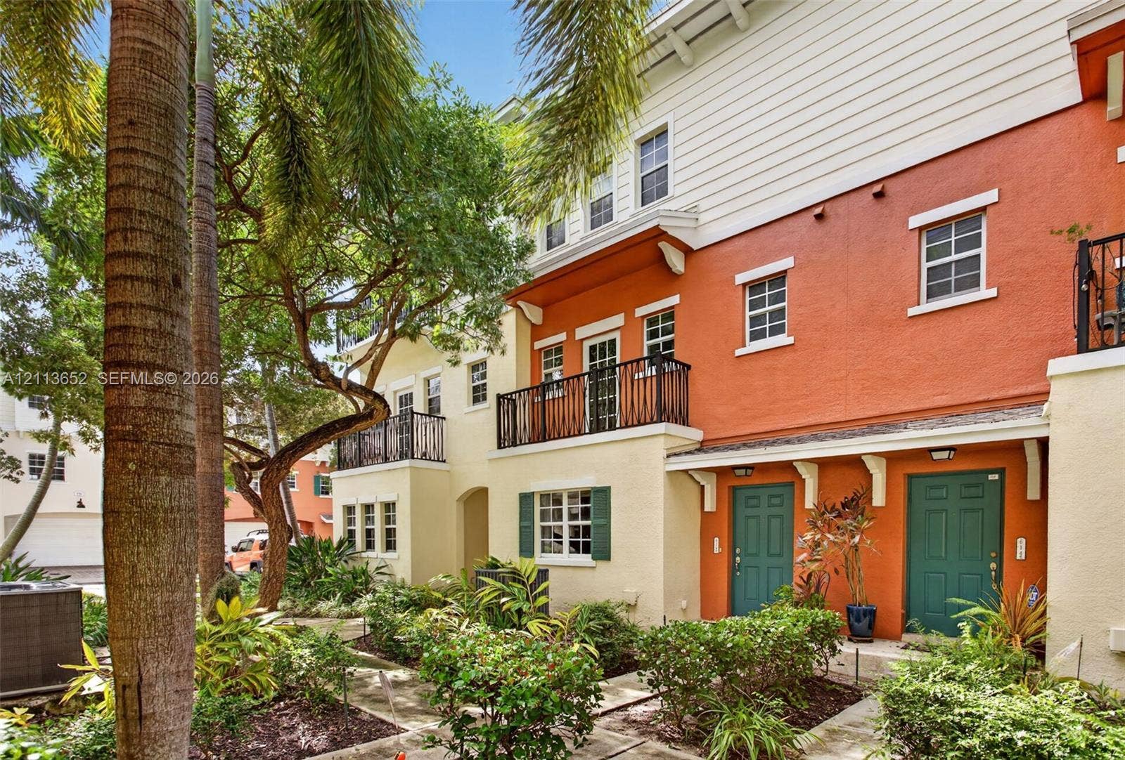 618 SW 1st Lane, Pompano Beach, FL 33060 Multi-level exterior featuring stucco siding, iron-railed balconies, double-hung windows with exterior shutters, and mature tropical landscaping