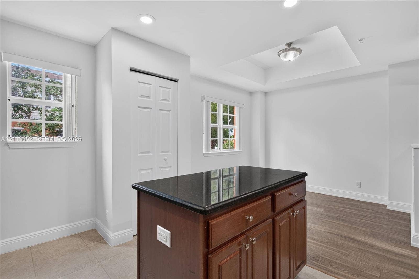618 SW 1st Lane, Pompano Beach, FL 33060 Kitchen island with a dark stone countertop and wood-finish cabinetry, recessed ceiling lighting, tray ceiling detail, dual-pane windows, and wood-finish flooring