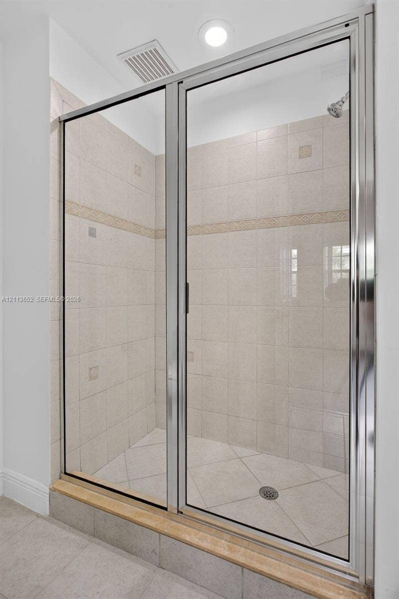618 SW 1st Lane, Pompano Beach, FL 33060 Walk-in shower enclosure featuring a polished metal frame, light-toned ceramic wall tiling with a decorative border inlay, diamond-patterned floor tile, and a raised stone threshold