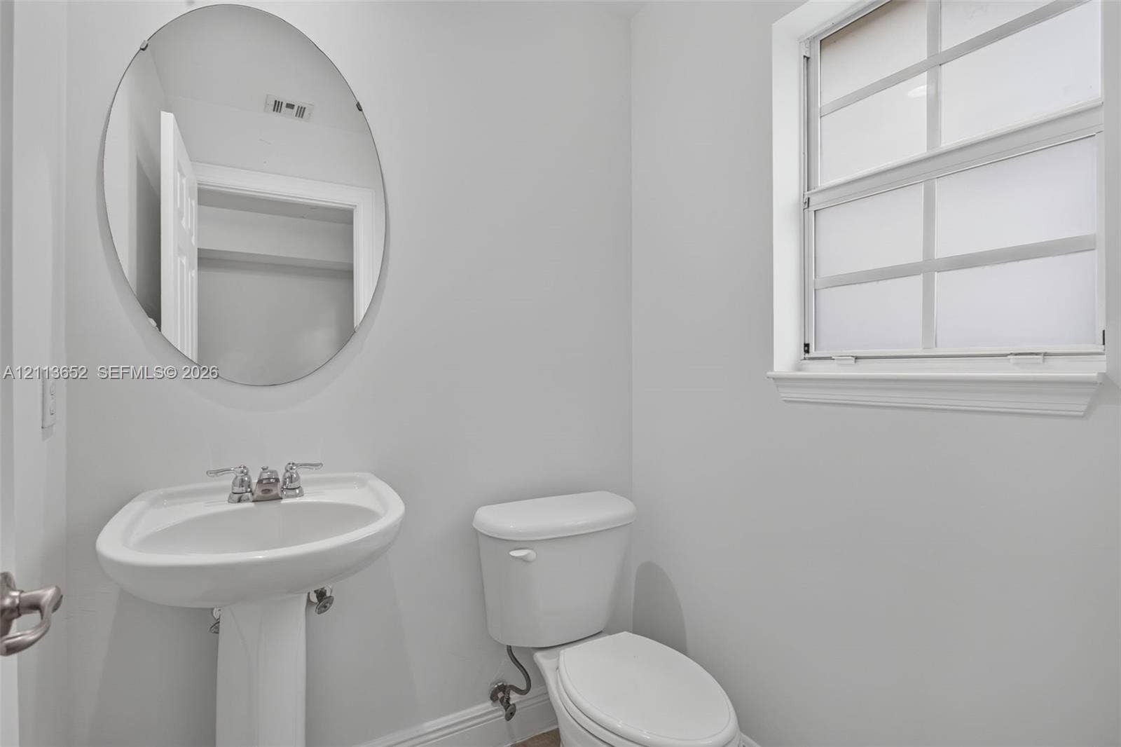 618 SW 1st Lane, Pompano Beach, FL 33060 White pedestal sink with chrome faucet, oval frameless mirror, and multi-pane window with interior muntins