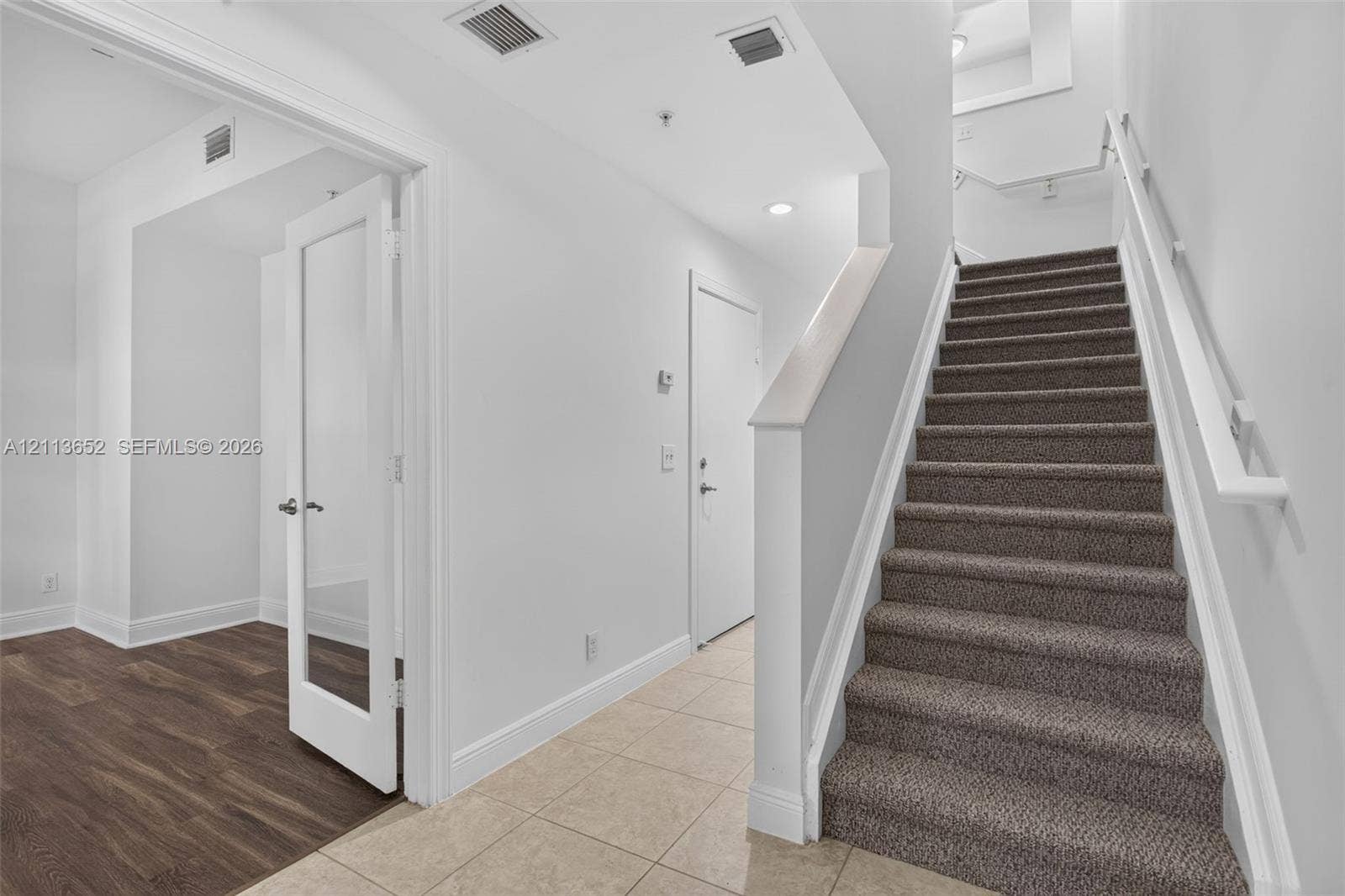 618 SW 1st Lane, Pompano Beach, FL 33060 Foyer featuring neutral tile flooring, staircase with carpeted treads, and a glass-panel interior door opening to wood-finish flooring