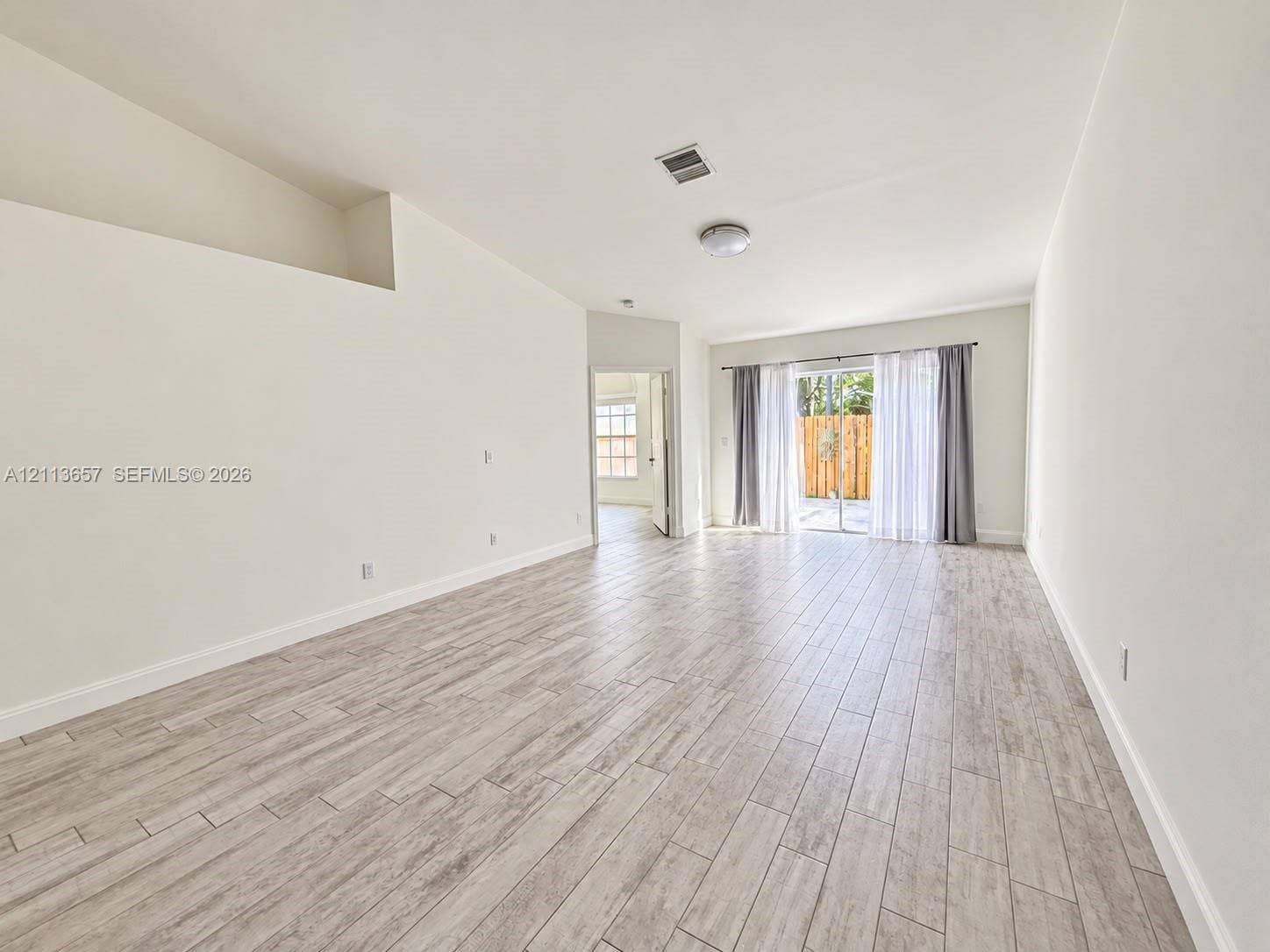 Open-concept room featuring vaulted ceilings, wood-finish tile flooring, and sliding glass doors
