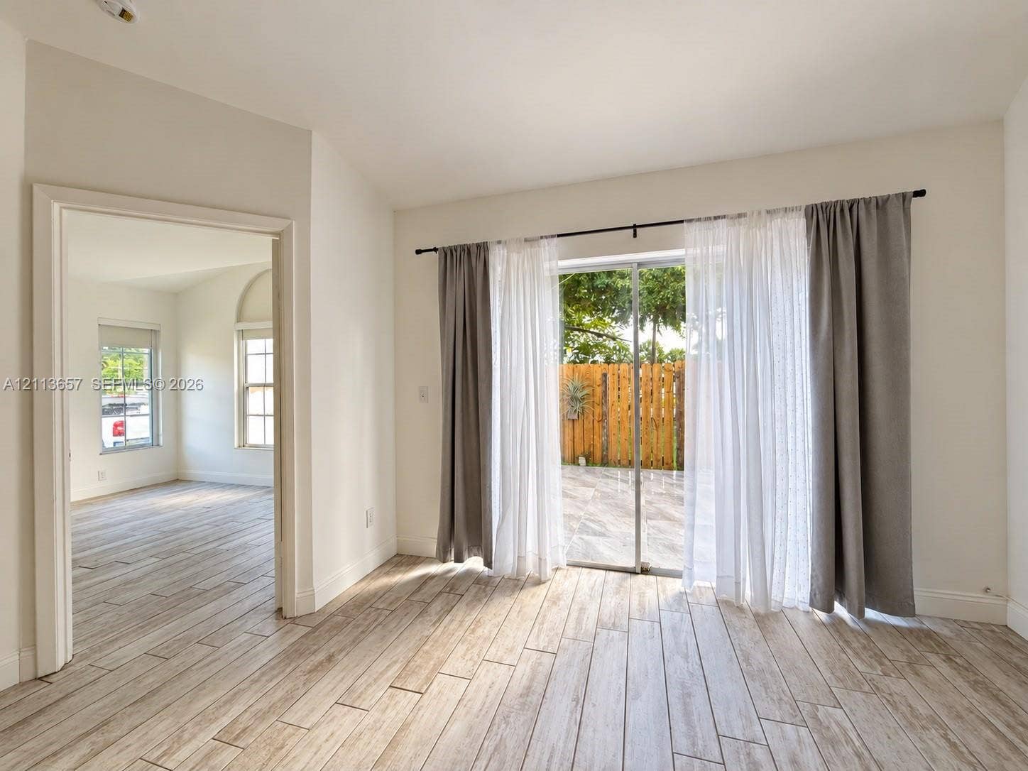 Wood-finish tile flooring throughout, neutral interior paint, and sliding glass doors with exterior access to a paved patio