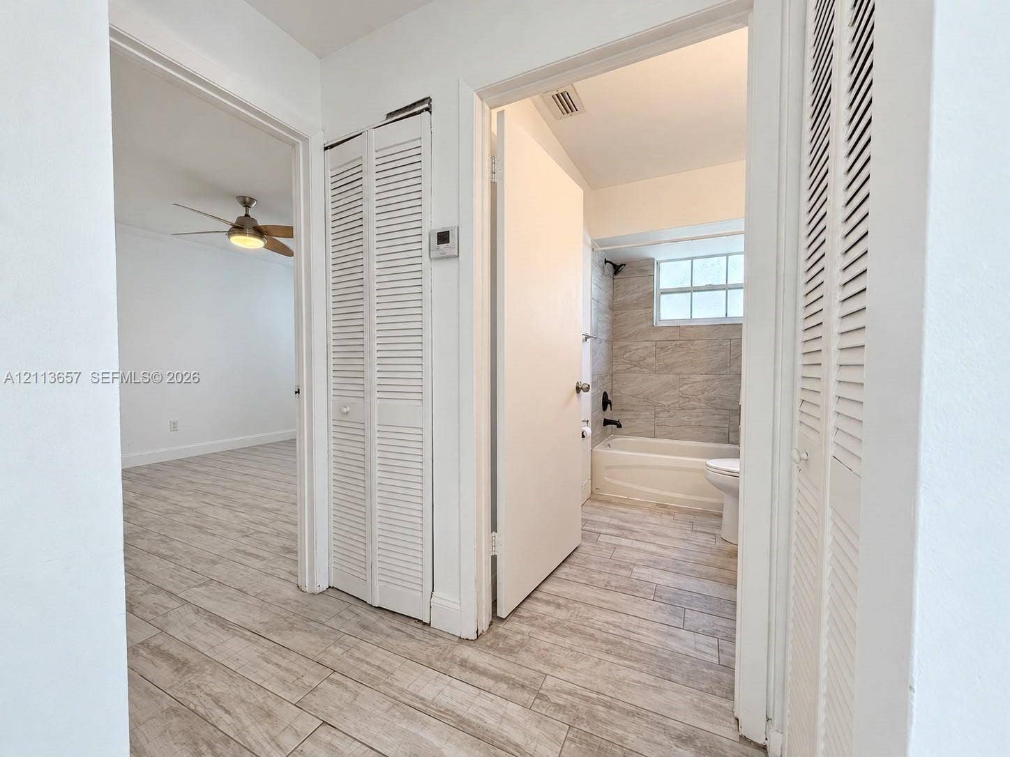 Wood-finish flooring throughout, louvered closet doors, and a bathroom featuring full-height stone-finish wall tile, a built-in shower-tub combination, and matte black hardware