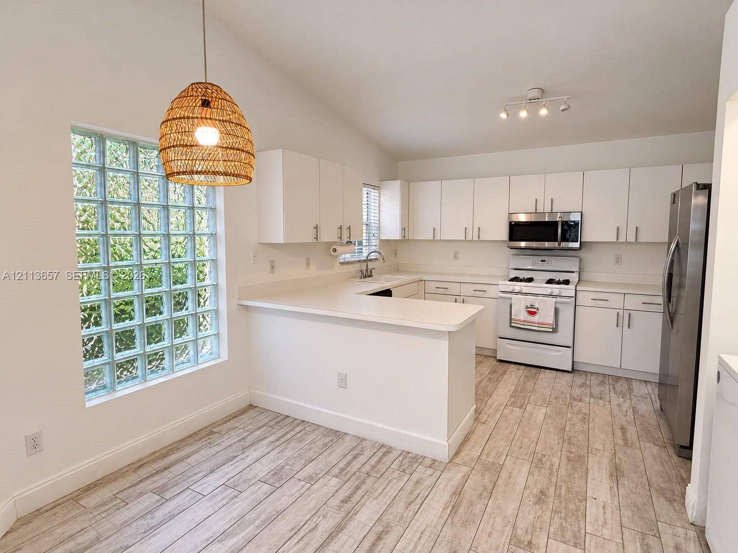 Kitchen featuring white cabinetry, wood-finish flooring, glass block window, and stainless steel appliances