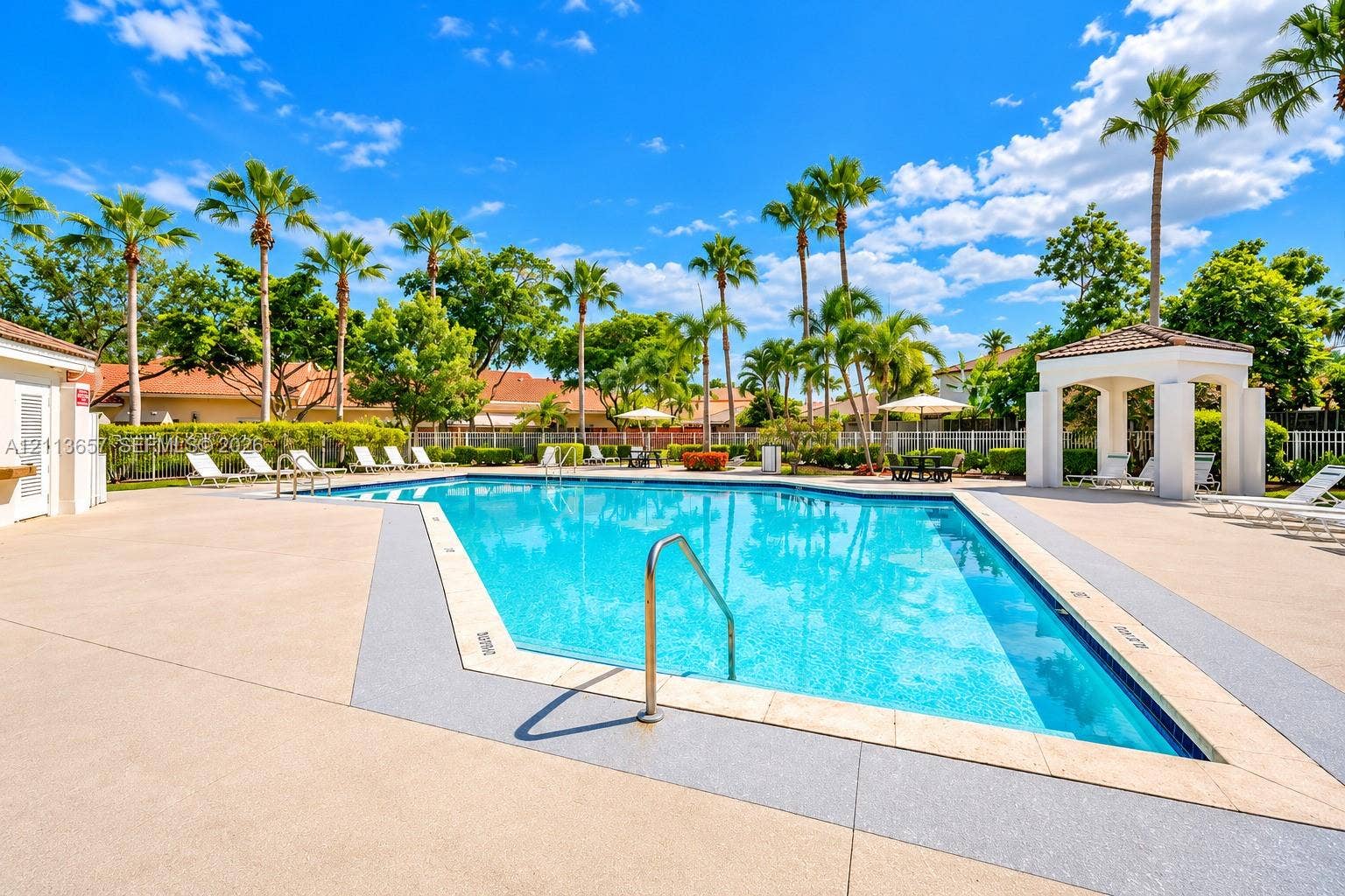 Swimming pool with surrounding concrete deck, metal handrail, and covered pavilion