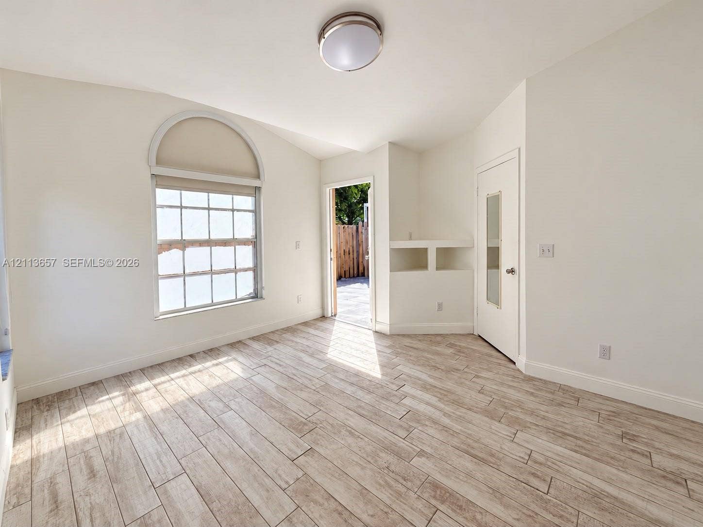 Room featuring wood-finish tile flooring, vaulted ceilings, a prominent arched window, built-in shelving, and a glass-paneled door