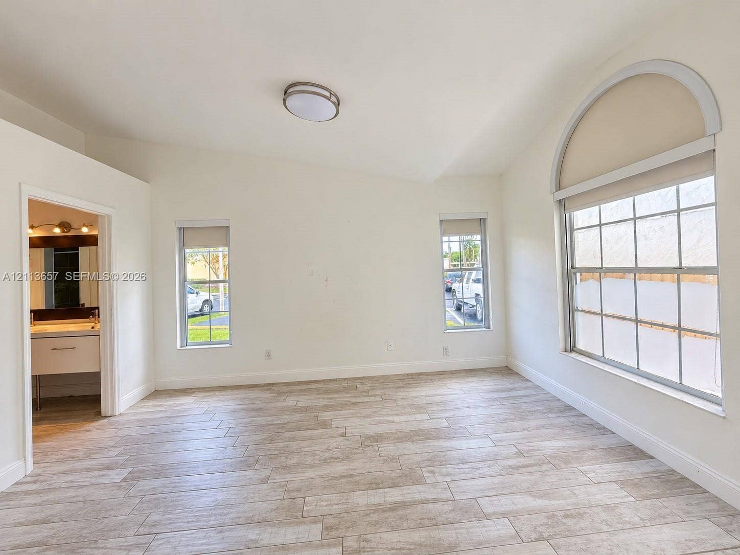 Room featuring vaulted ceilings, neutral-tone wood-finish flooring, and a prominent arched window