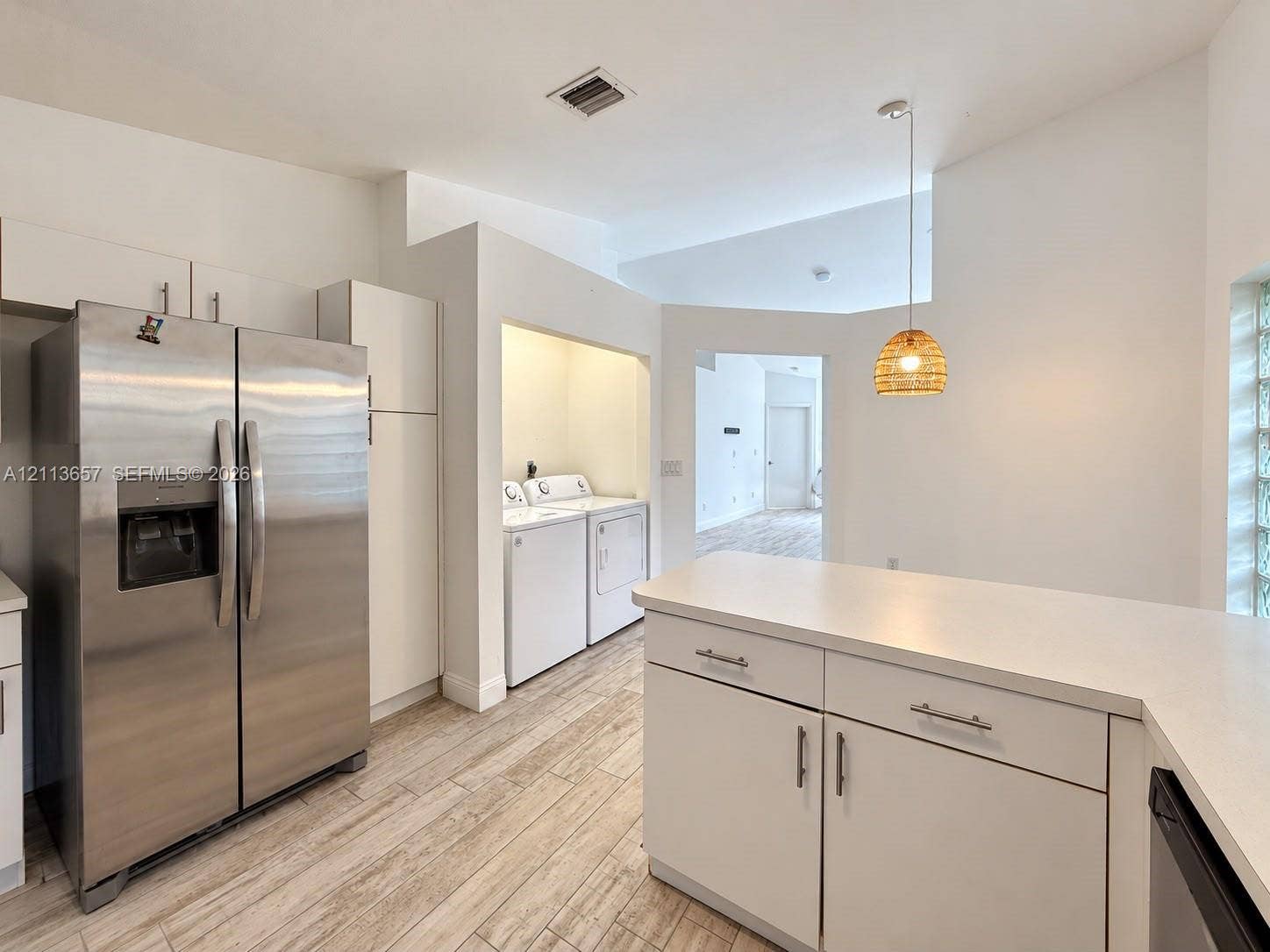 Kitchen featuring stainless steel side-by-side refrigerator, white cabinetry with silver-tone hardware, solid-surface countertops, wood-finish tile flooring, and glass block window detailing