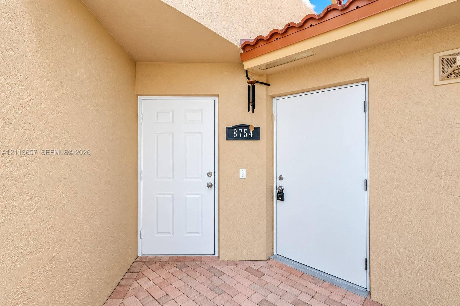 Stucco exterior entry featuring a brick-paver walkway, recessed entryway, and clay-tile roof trim