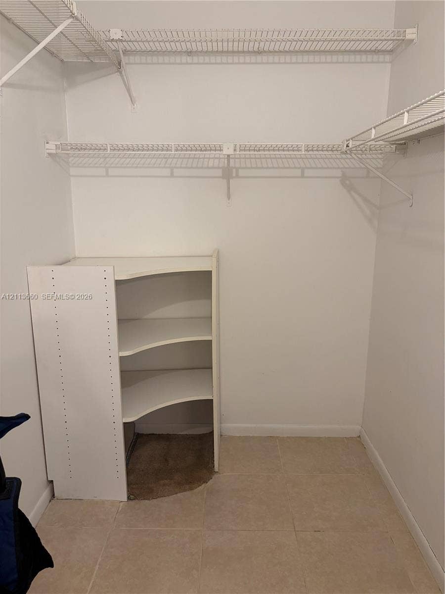 Walk-in closet featuring dual-tier wire shelving and built-in corner storage unit with tile flooring