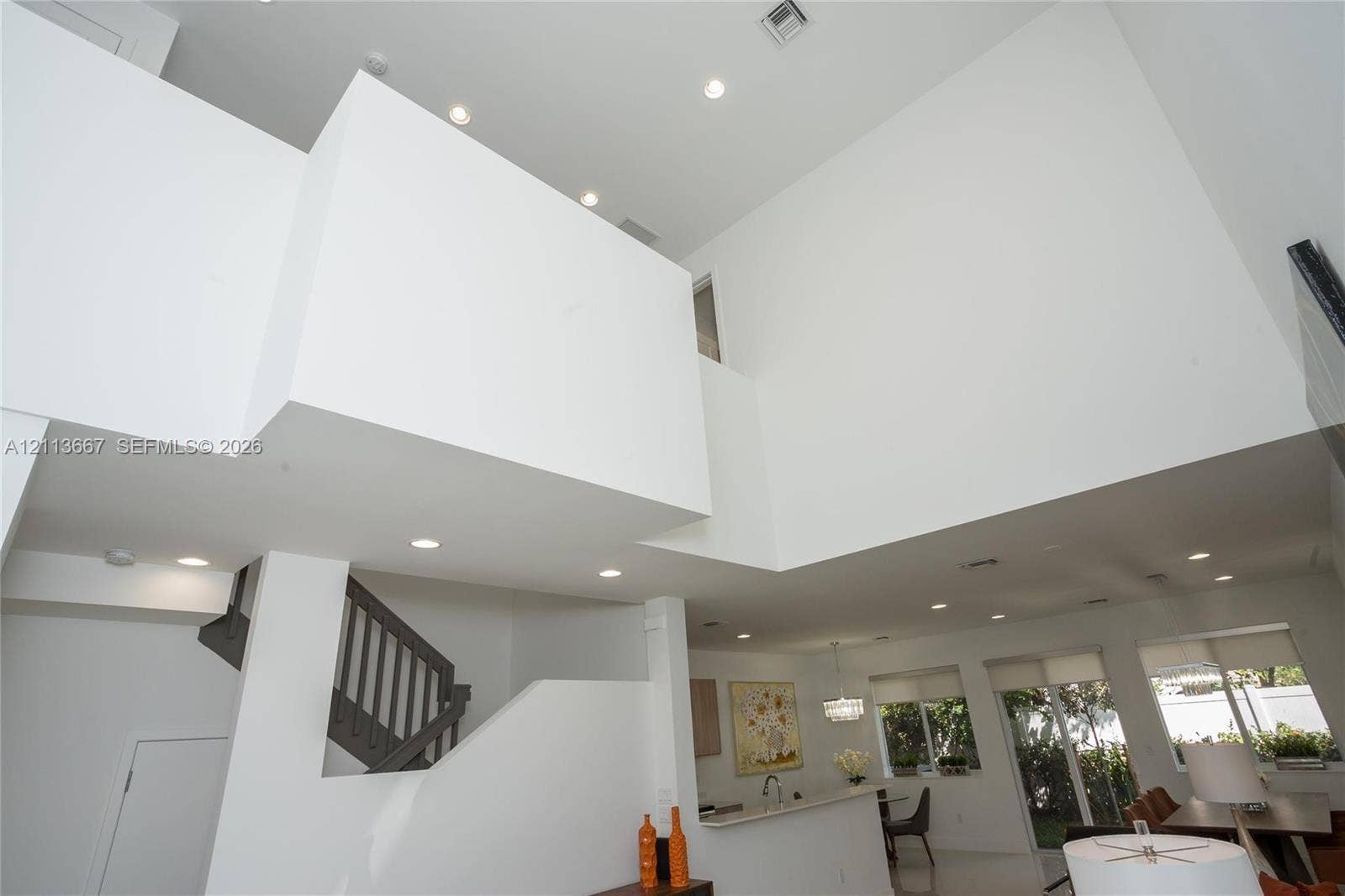 Double-height volume ceiling, recessed lighting, and staircase with dark-toned balustrades
