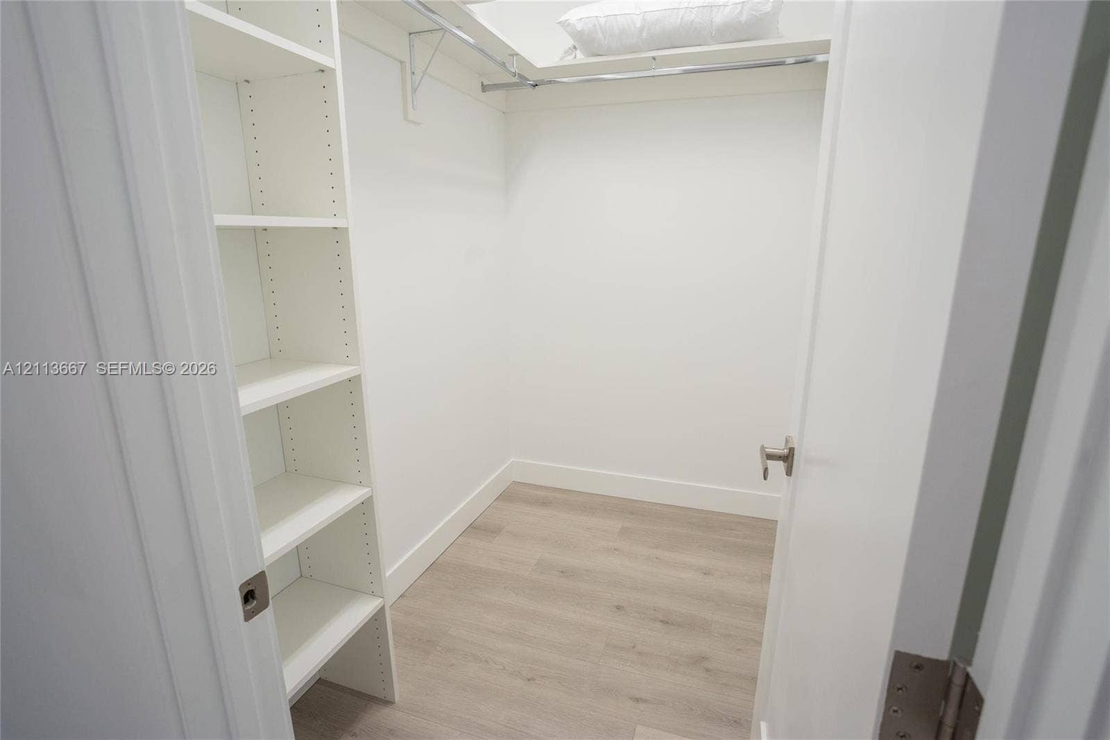 Walk-in closet featuring white built-in shelving, wood-finish flooring, and a metal garment rod