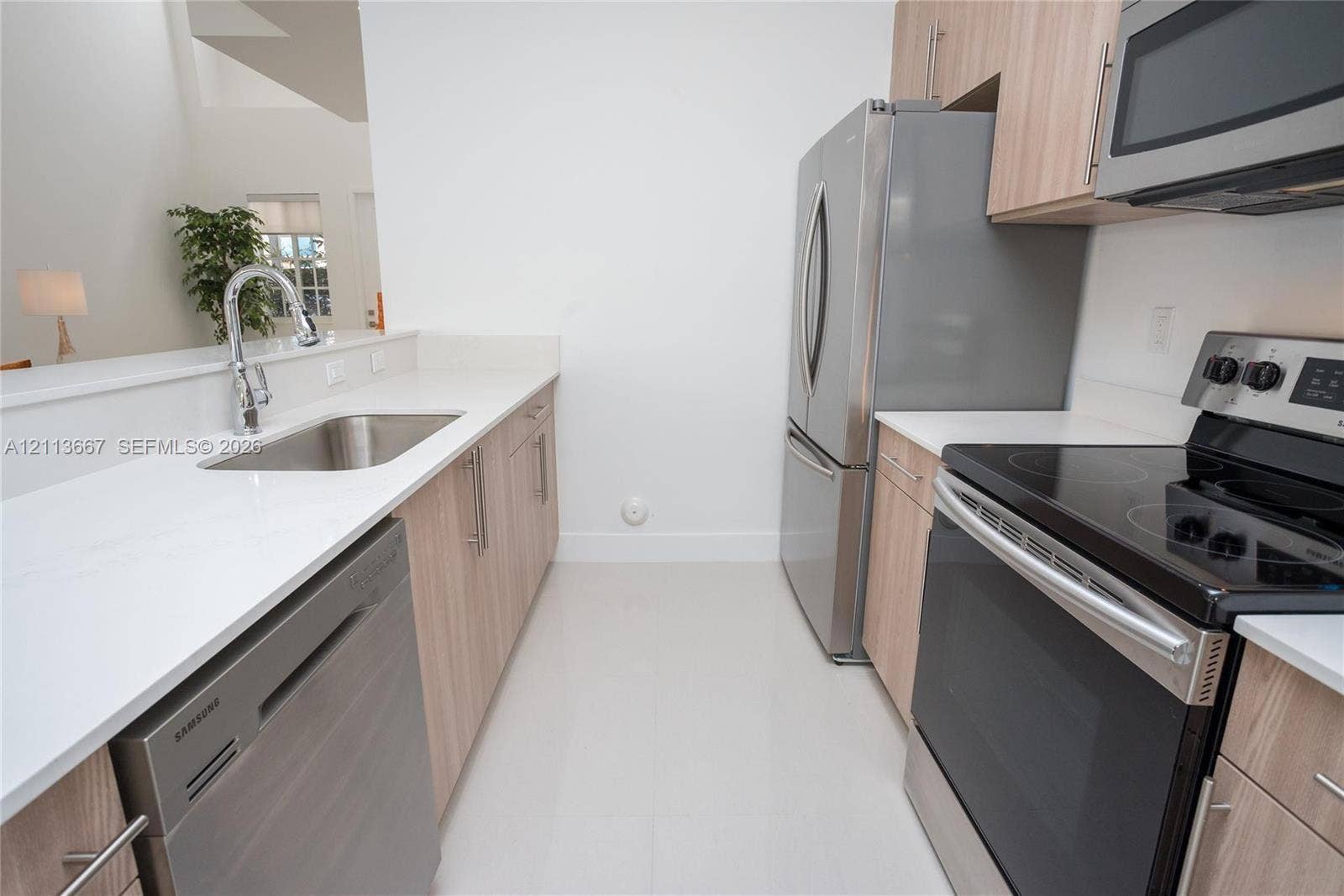 Kitchen featuring light wood-finish cabinetry, stainless steel appliances, solid surface countertops, a stainless steel under-mount sink with a pull-down faucet, and light-toned tile flooring