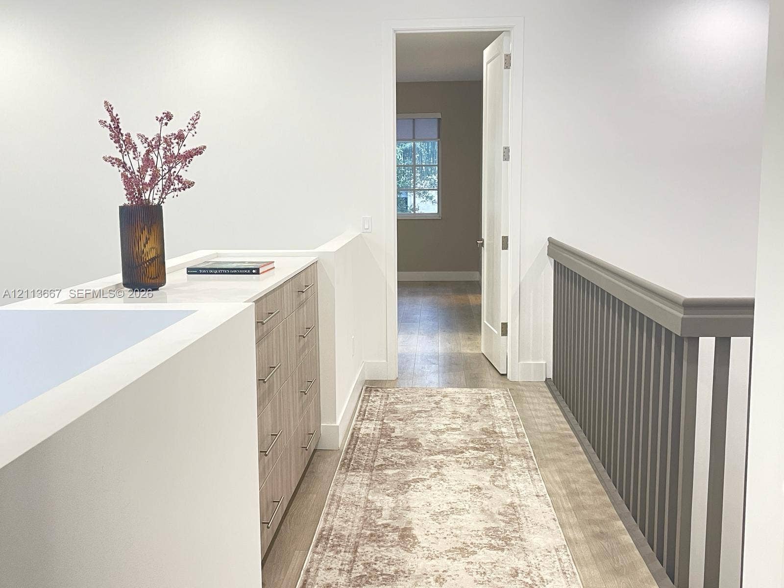 Built-in cabinetry featuring light wood-finish drawers, neutral countertop, wood-finish flooring, and painted spindle railing