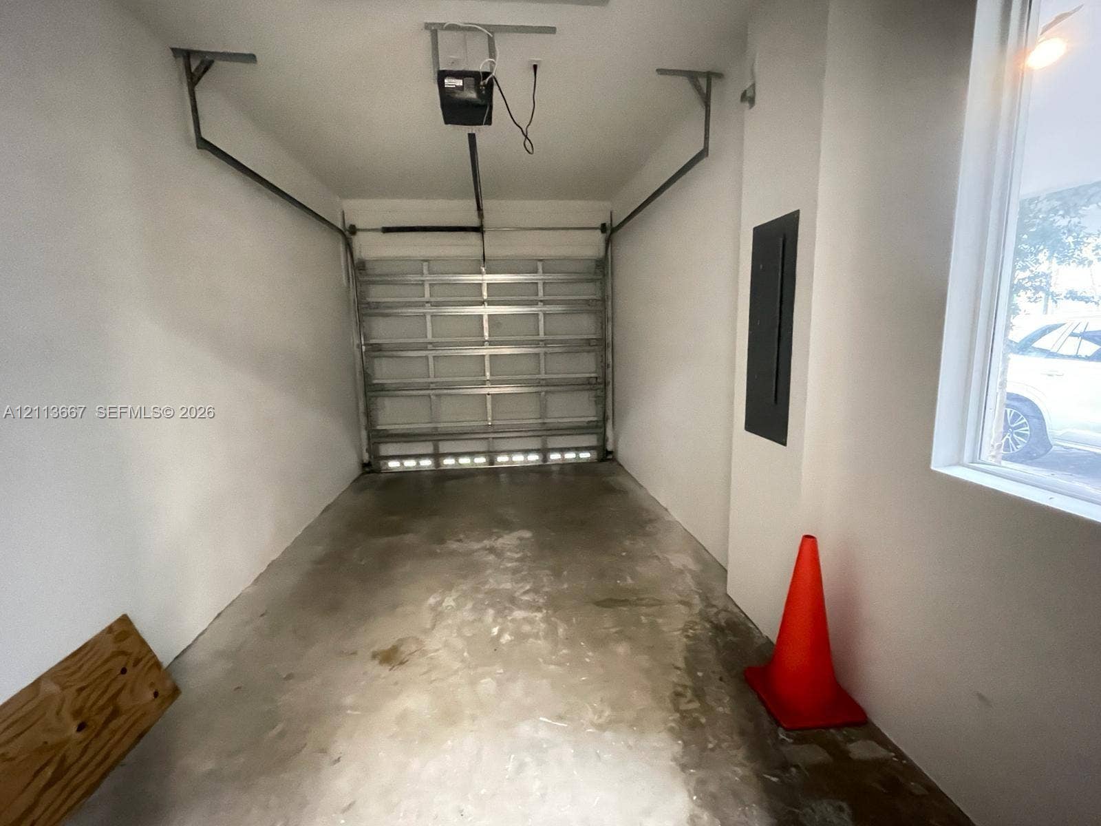 Single-car garage featuring a roll-up metal door, concrete flooring, smooth wall finishes, and an integrated electrical panel