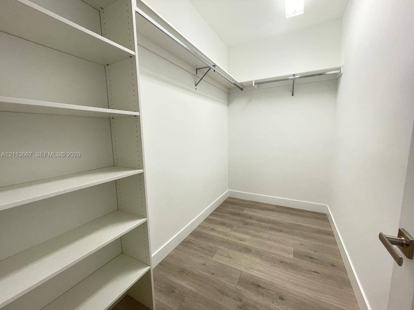 Storage area featuring white built-in shelving, metal garment rods, and wood-finish flooring